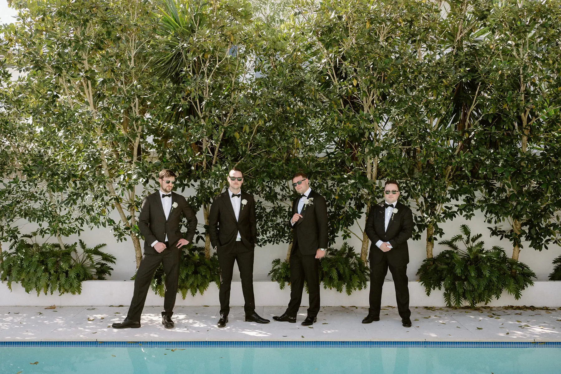 The groomsmen lined up along the pool in their black tie, Botanica Plantation House