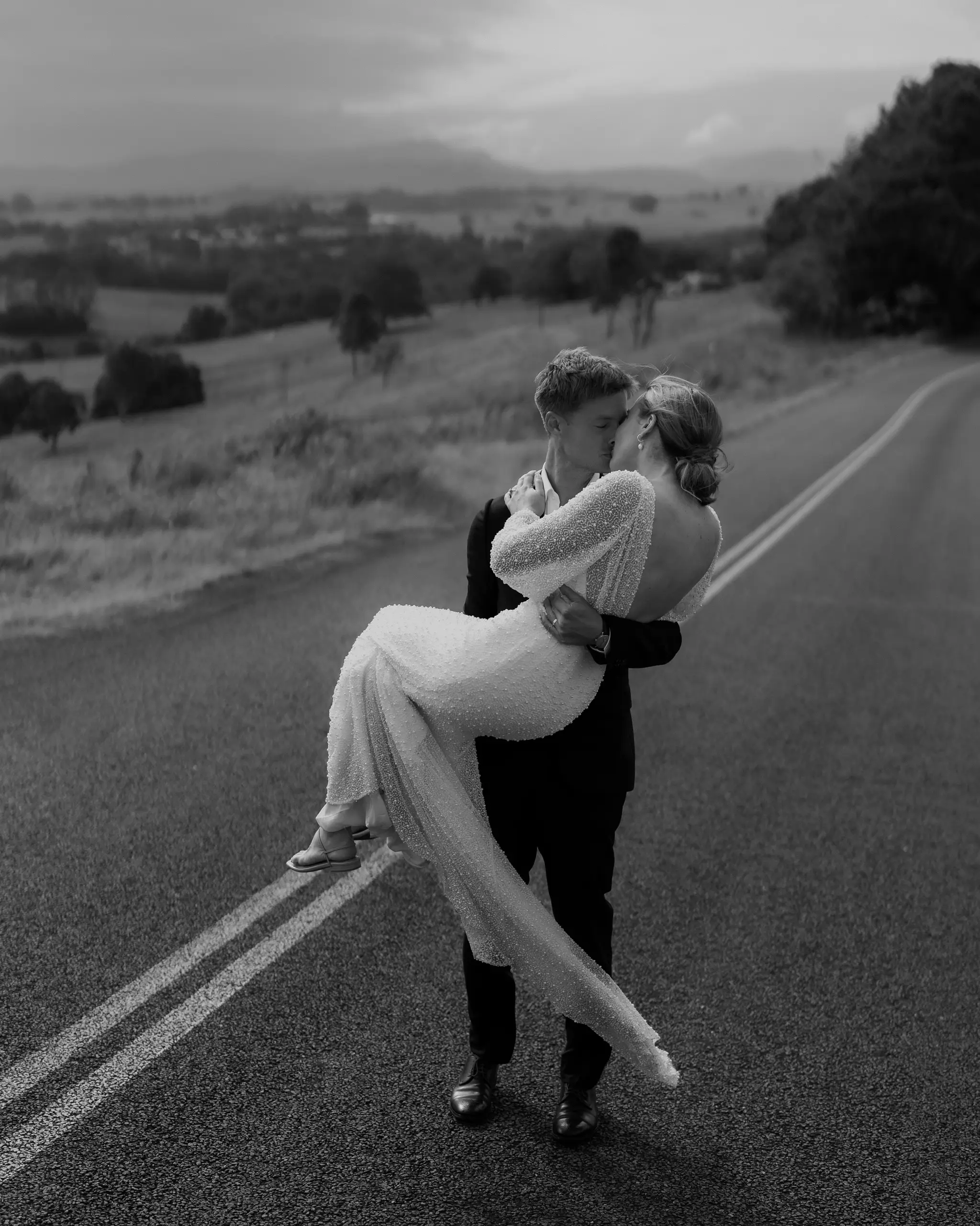 Groom lifting bride on an open country road
