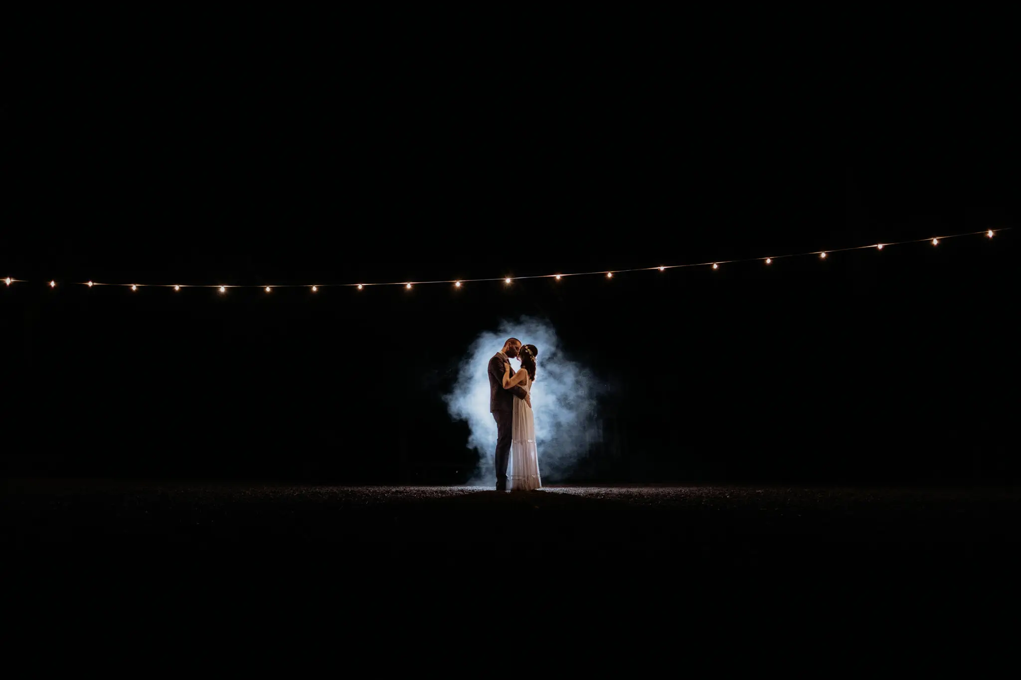 The couple small in torchlit mist beneath the night sky