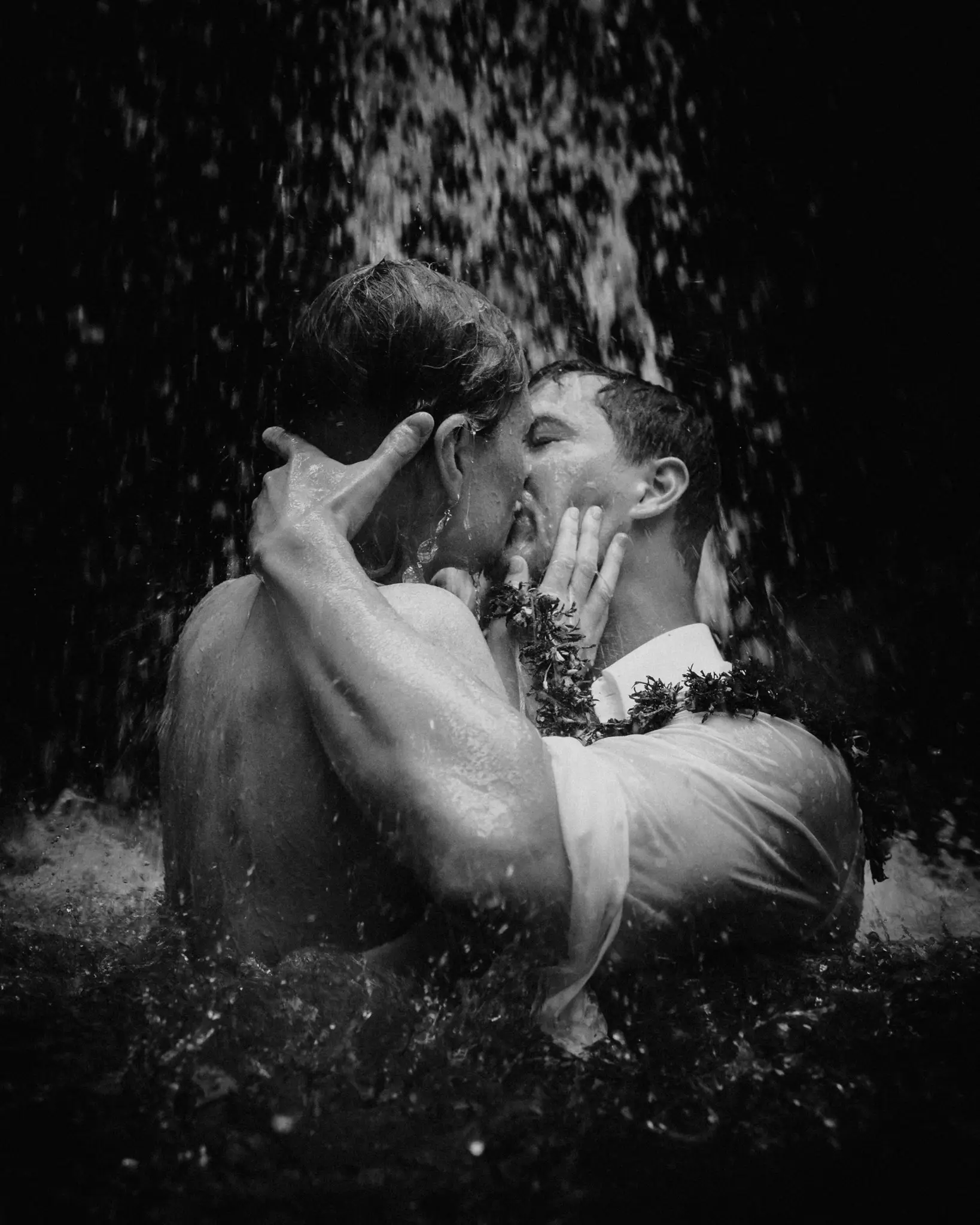 Couple kissing under falling rain at night, in black and white