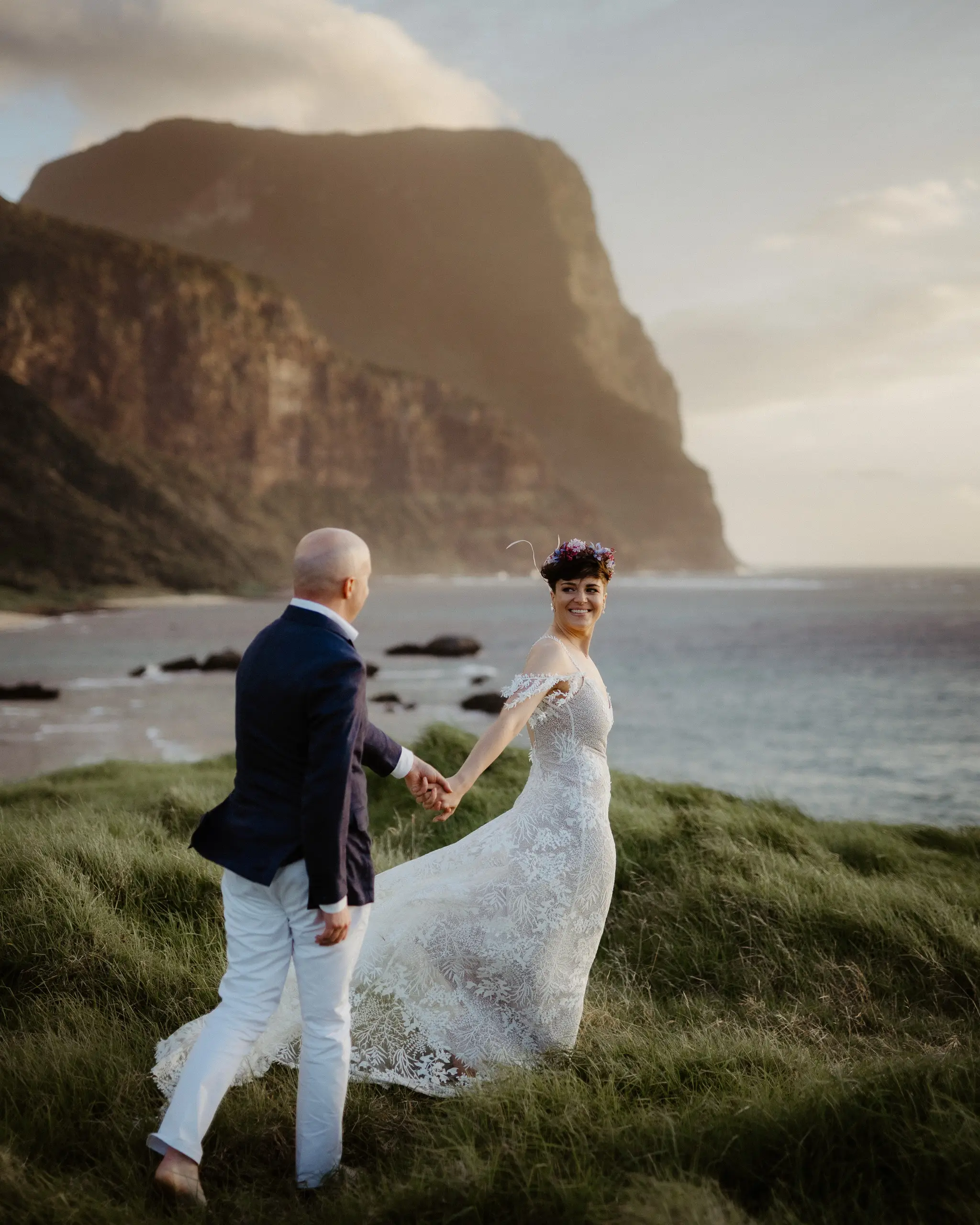 Couple hand in hand on a grassy headland beneath Mount Gower, Lord Howe Island