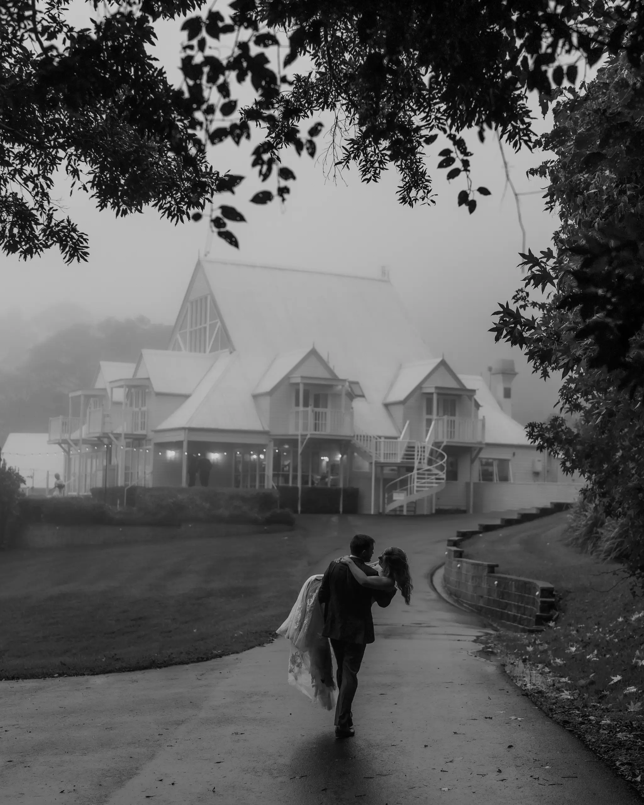 Couple walking a rain-soaked path toward a gabled house, in black and white