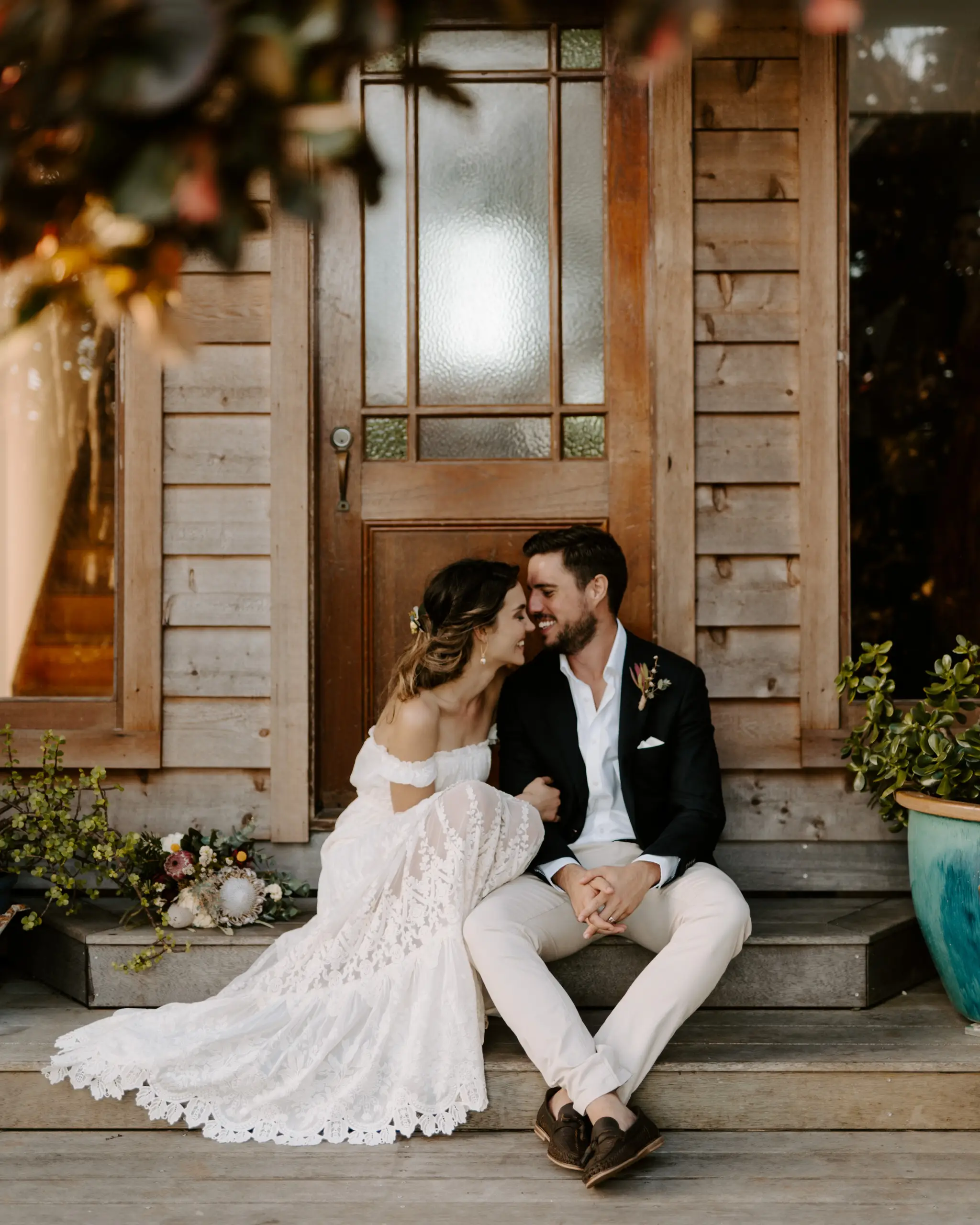 Bride and groom sitting together on the timber steps of a cottage doorway