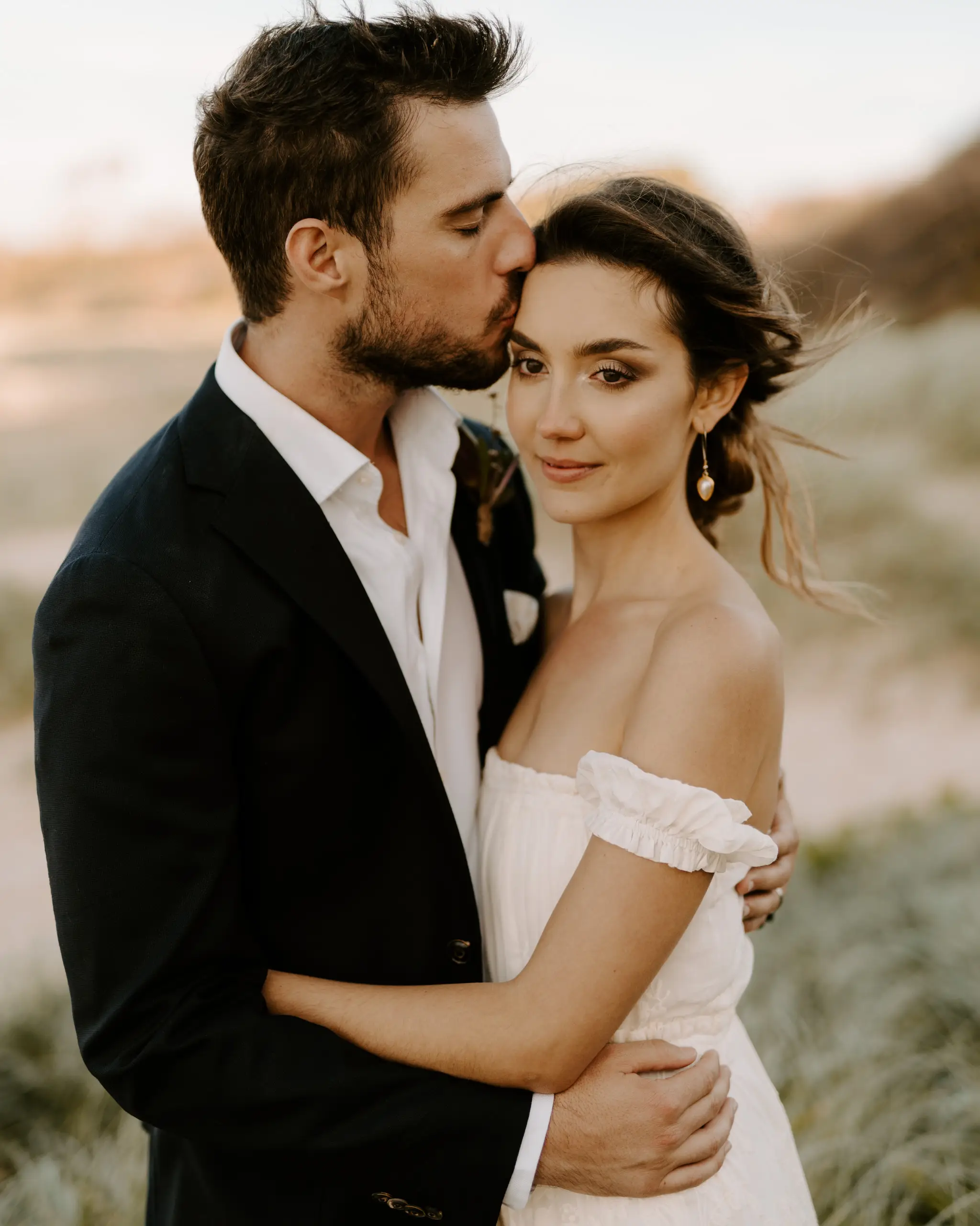 Groom kissing the bride's temple in the beach dunes