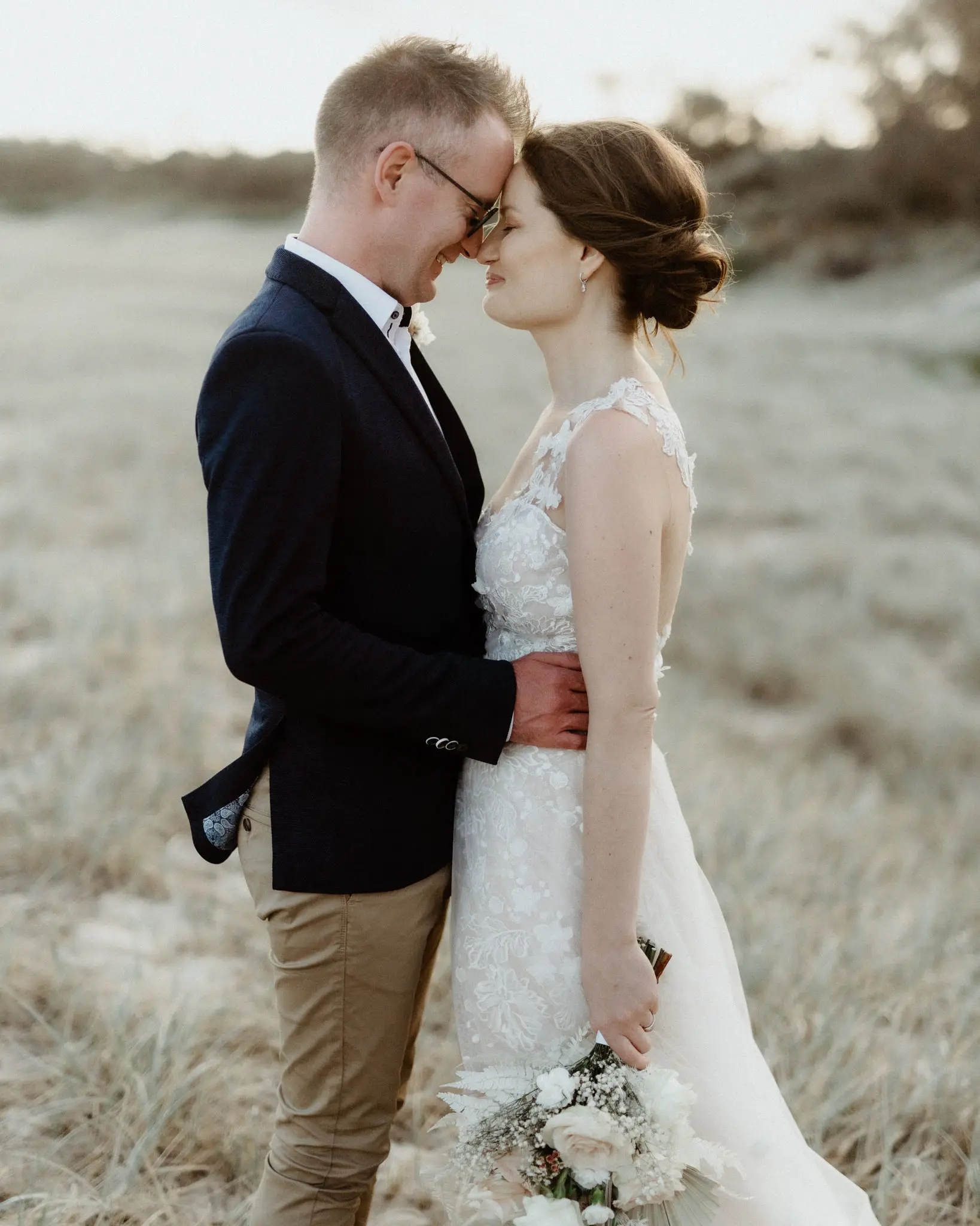 Bride and groom standing together in pale dune grass