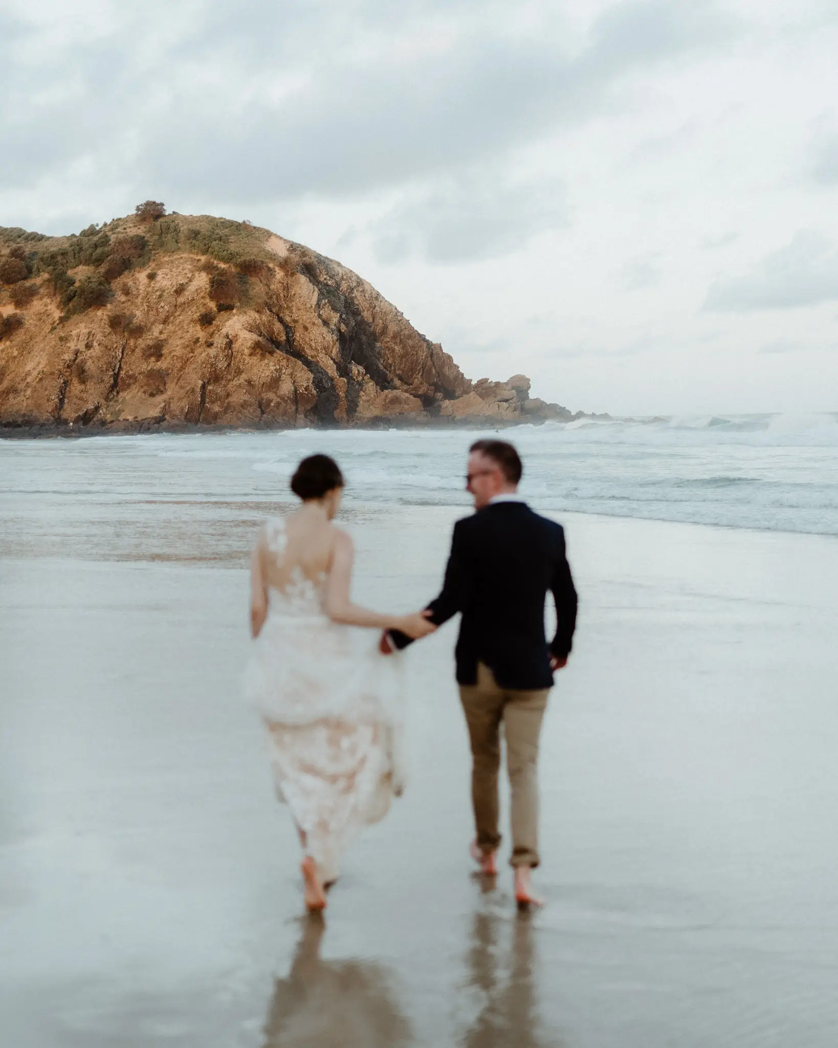 Couple hand in hand on wet sand below a headland