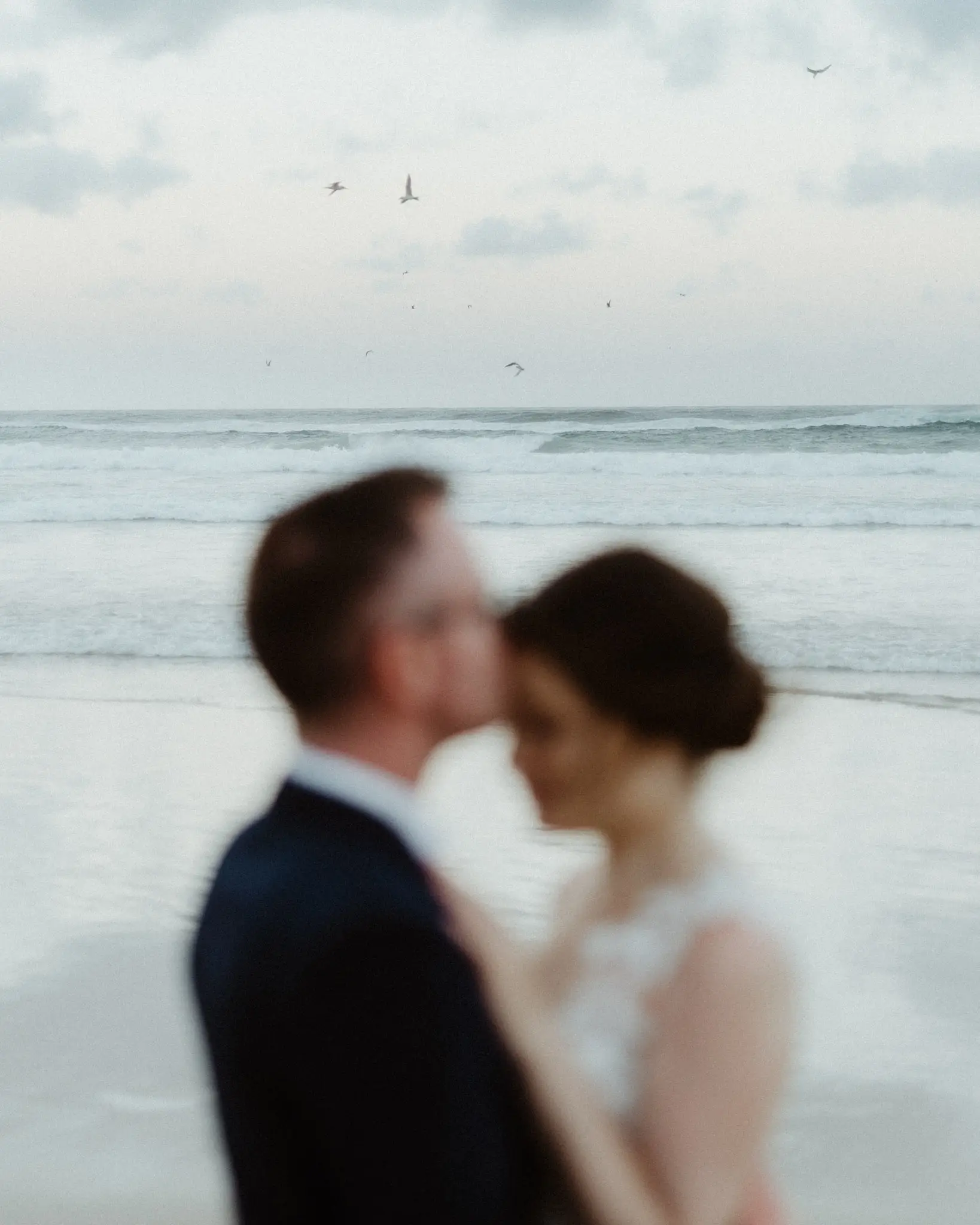 Soft-focus frame of the couple against the sea, birds overhead