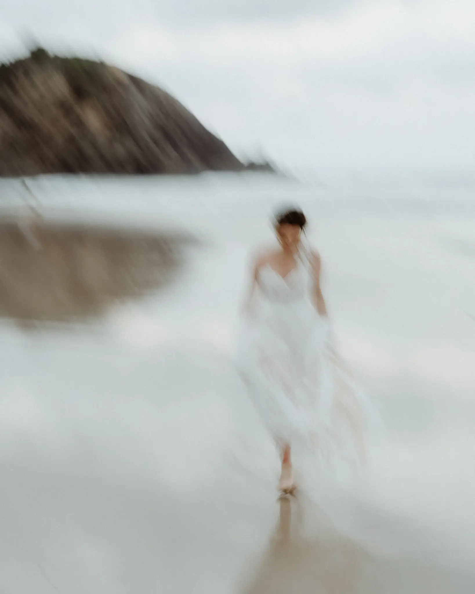 Bride walking the shoreline beneath a dark headland