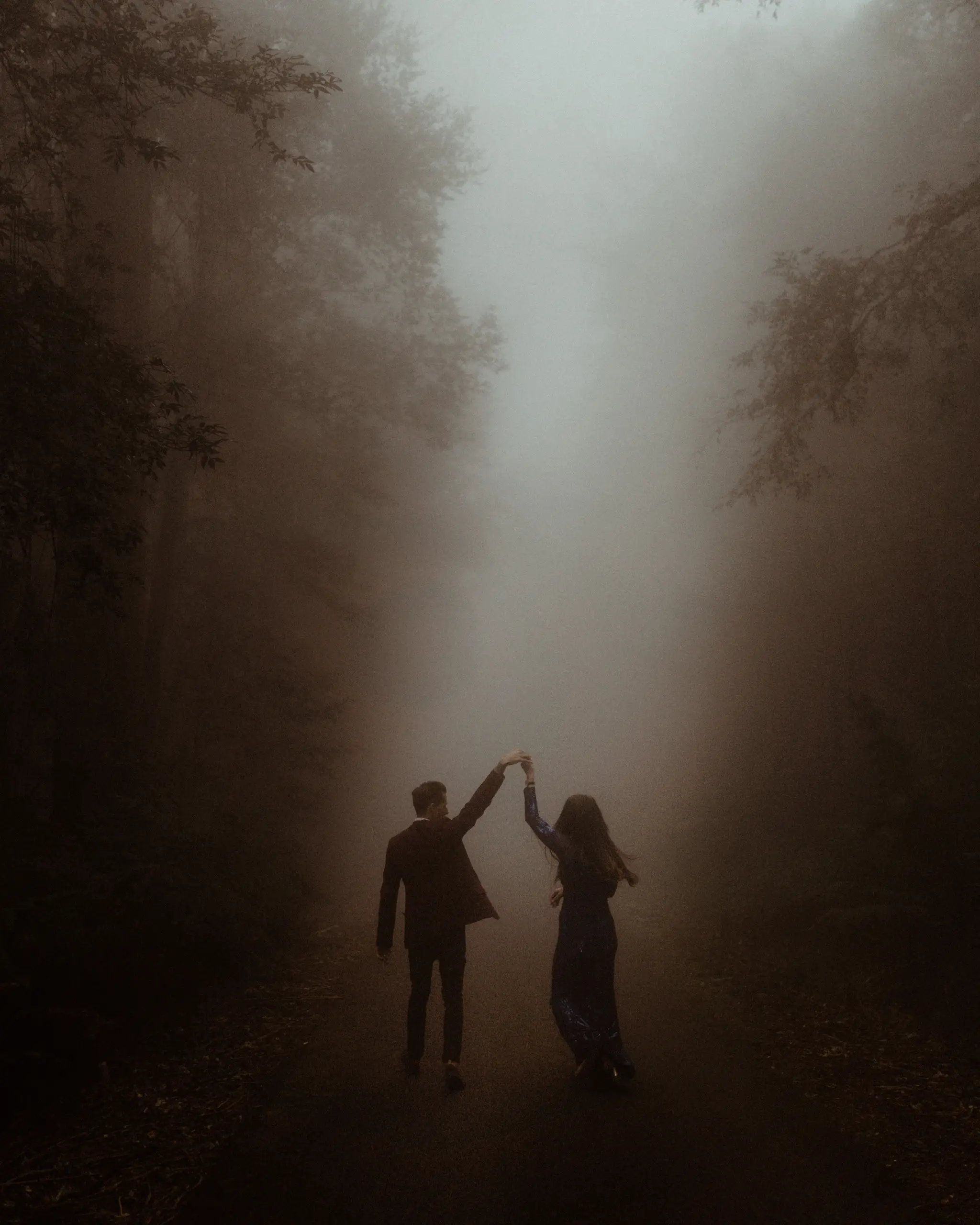 Couple with arms raised on a misty forest road