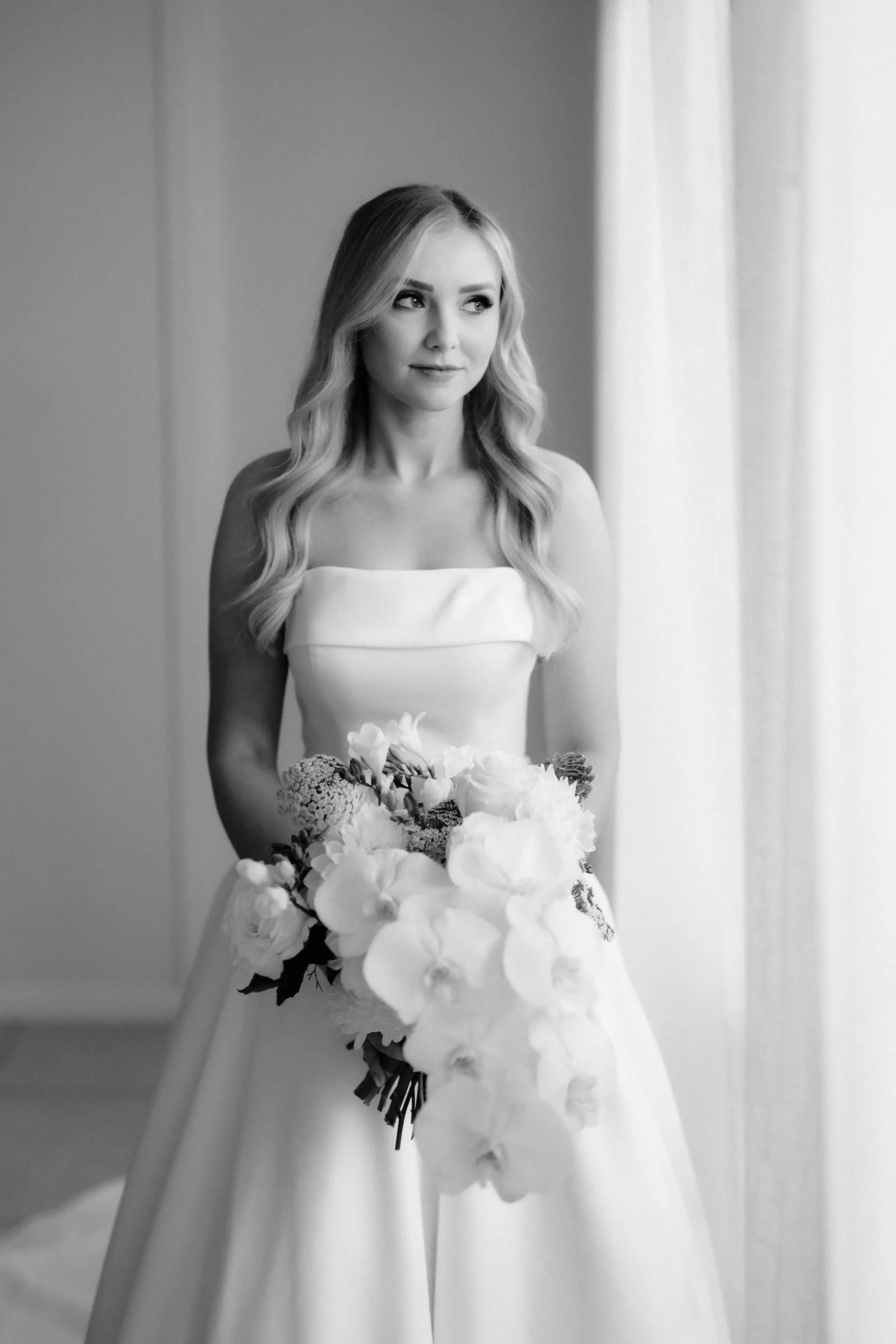 Bride at the window with a white orchid bouquet