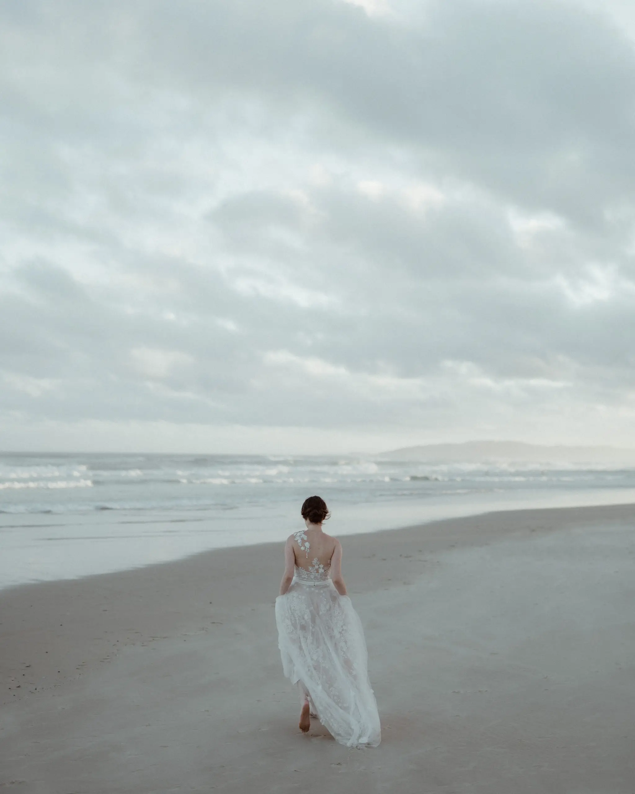 Bride alone on a vast beach under a towering sky