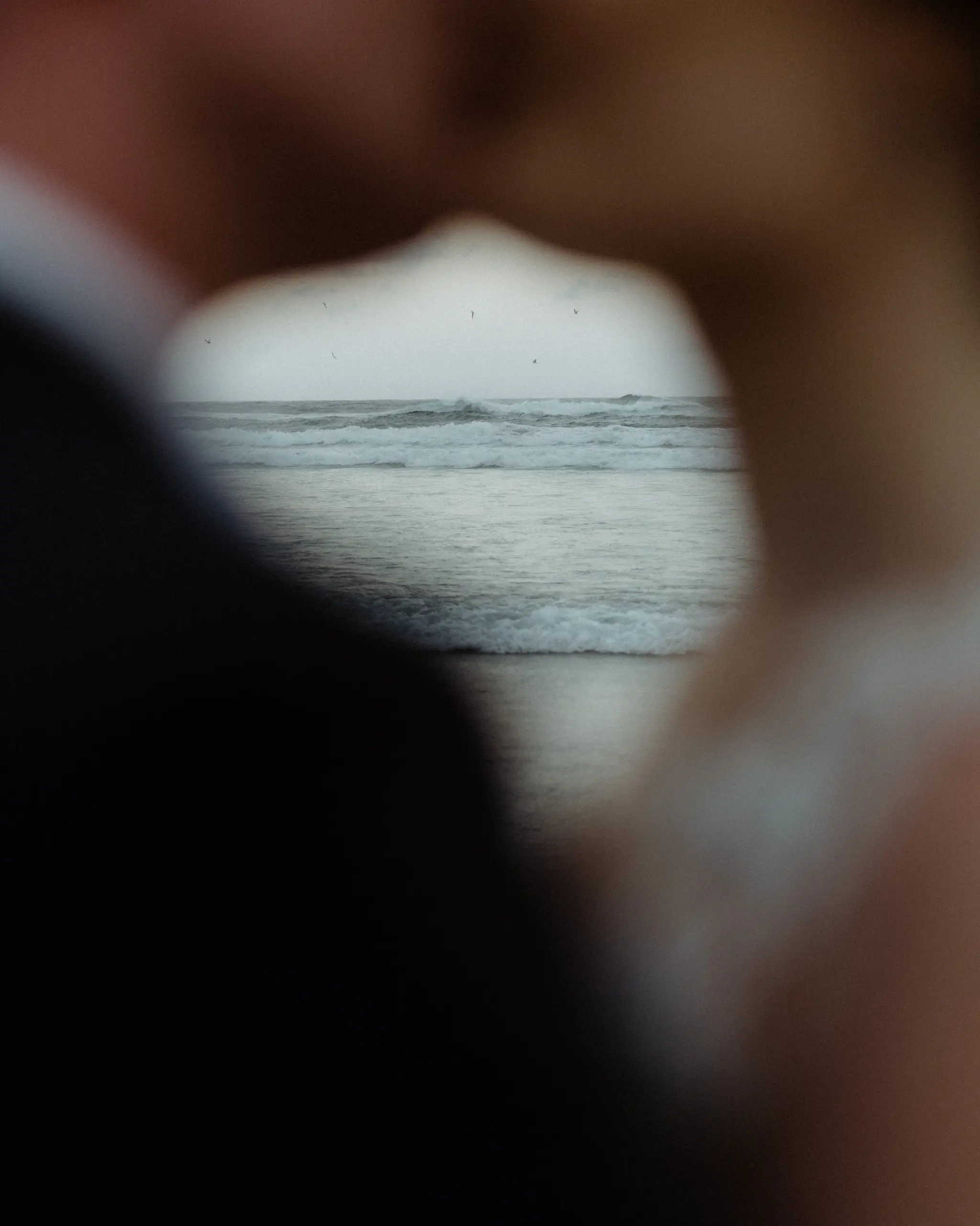 Frame through the groom's embrace to the sea beyond