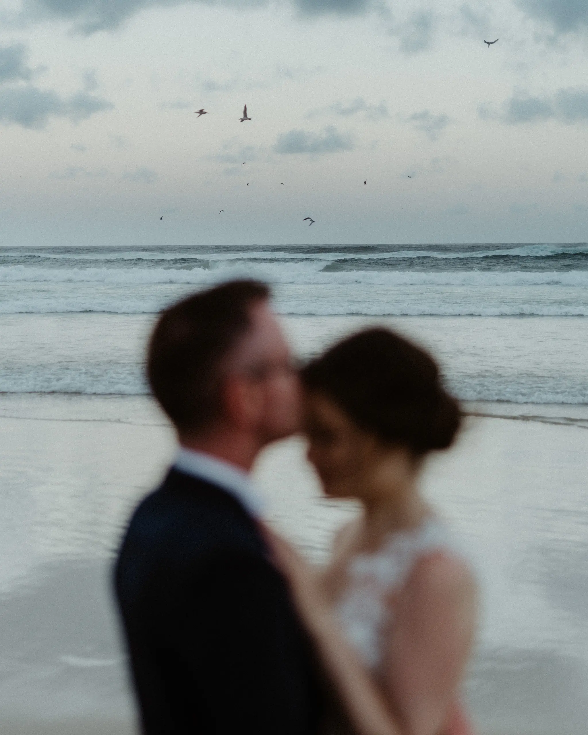 A soft kiss on the bride's hair, ocean behind