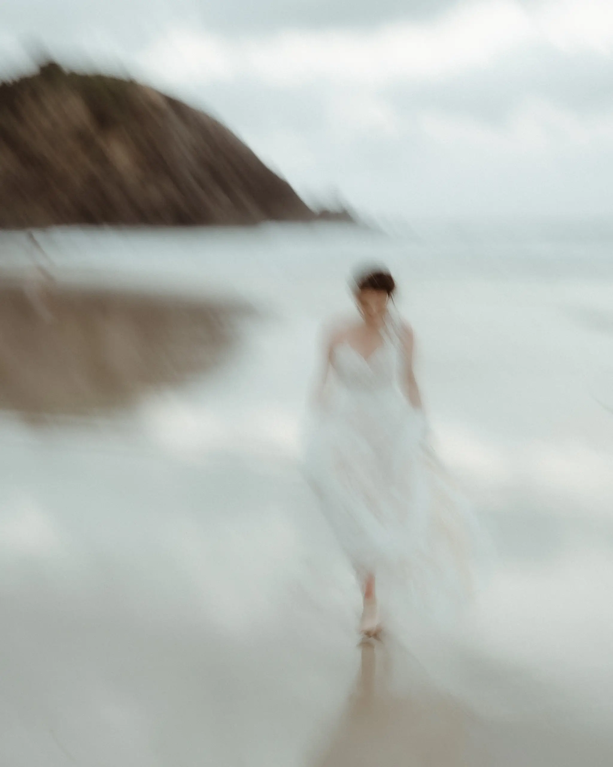 Bride walking the shoreline with the headland soft behind her
