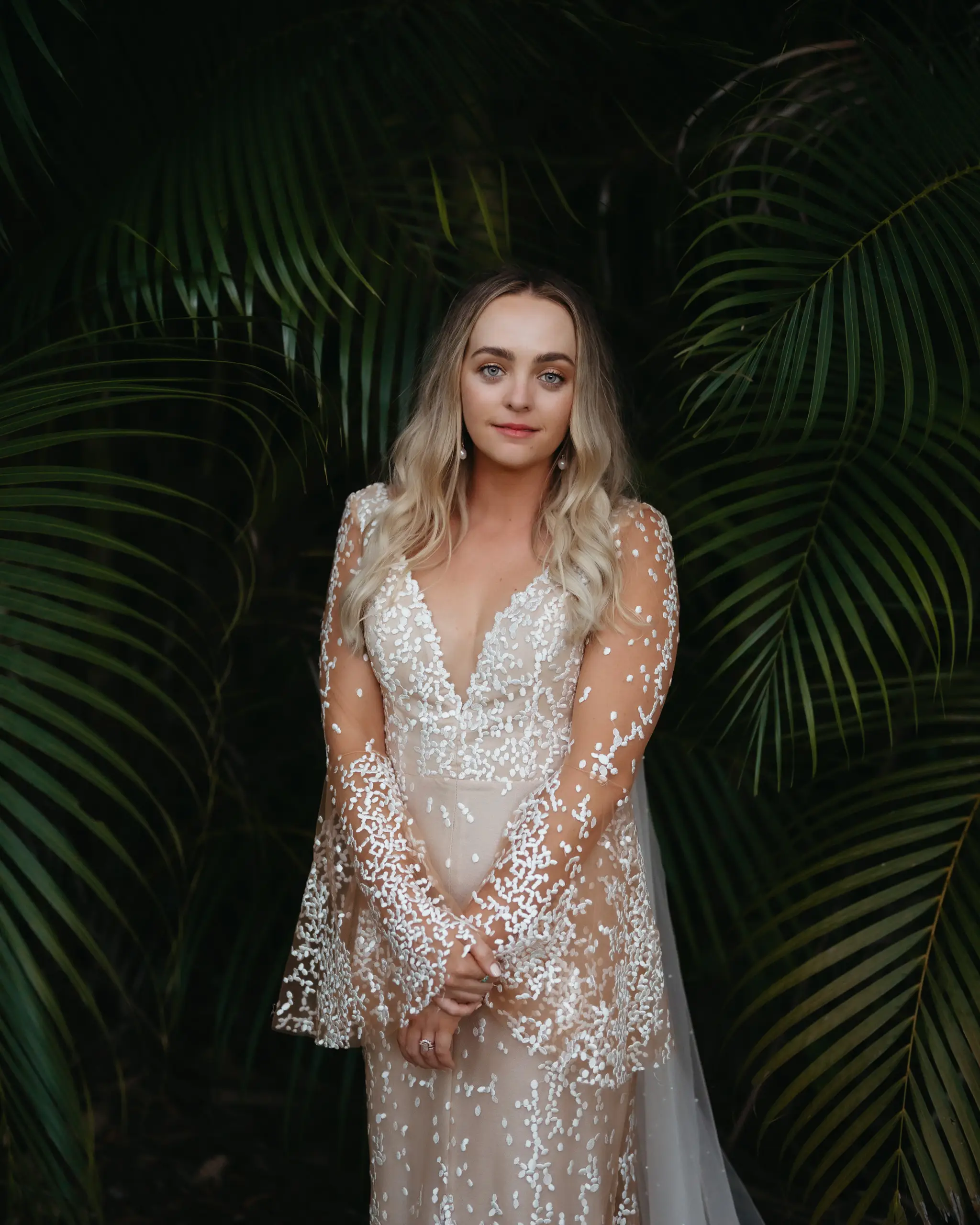 Bride in a beaded gown framed by palm fronds