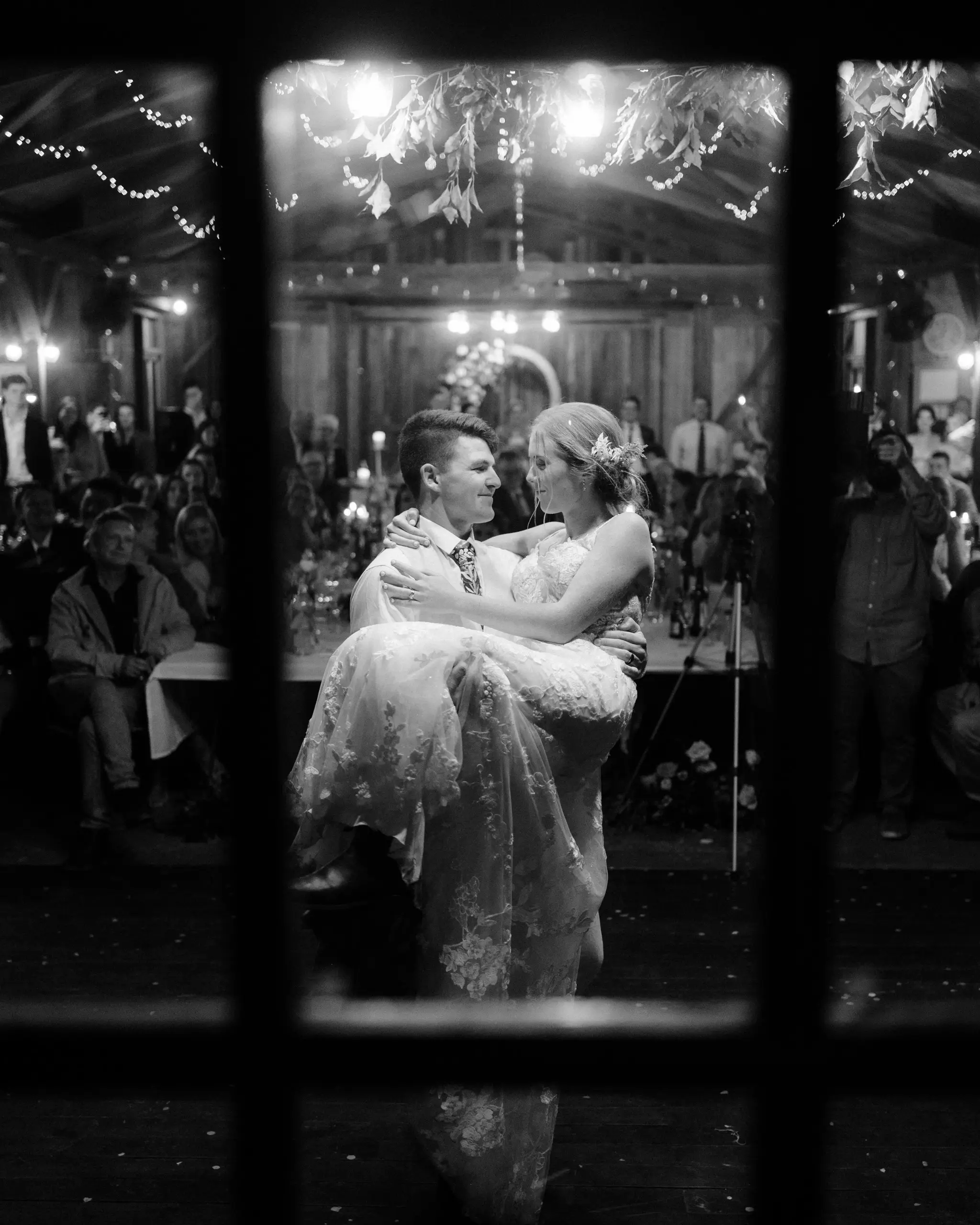 Groom lifting the bride on the dance floor, seen through the window, in black and white