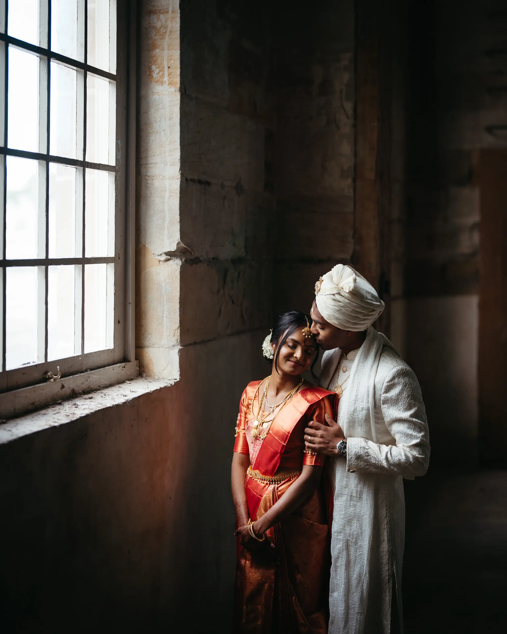 Couple in sherwani and red sari lit by a warehouse window