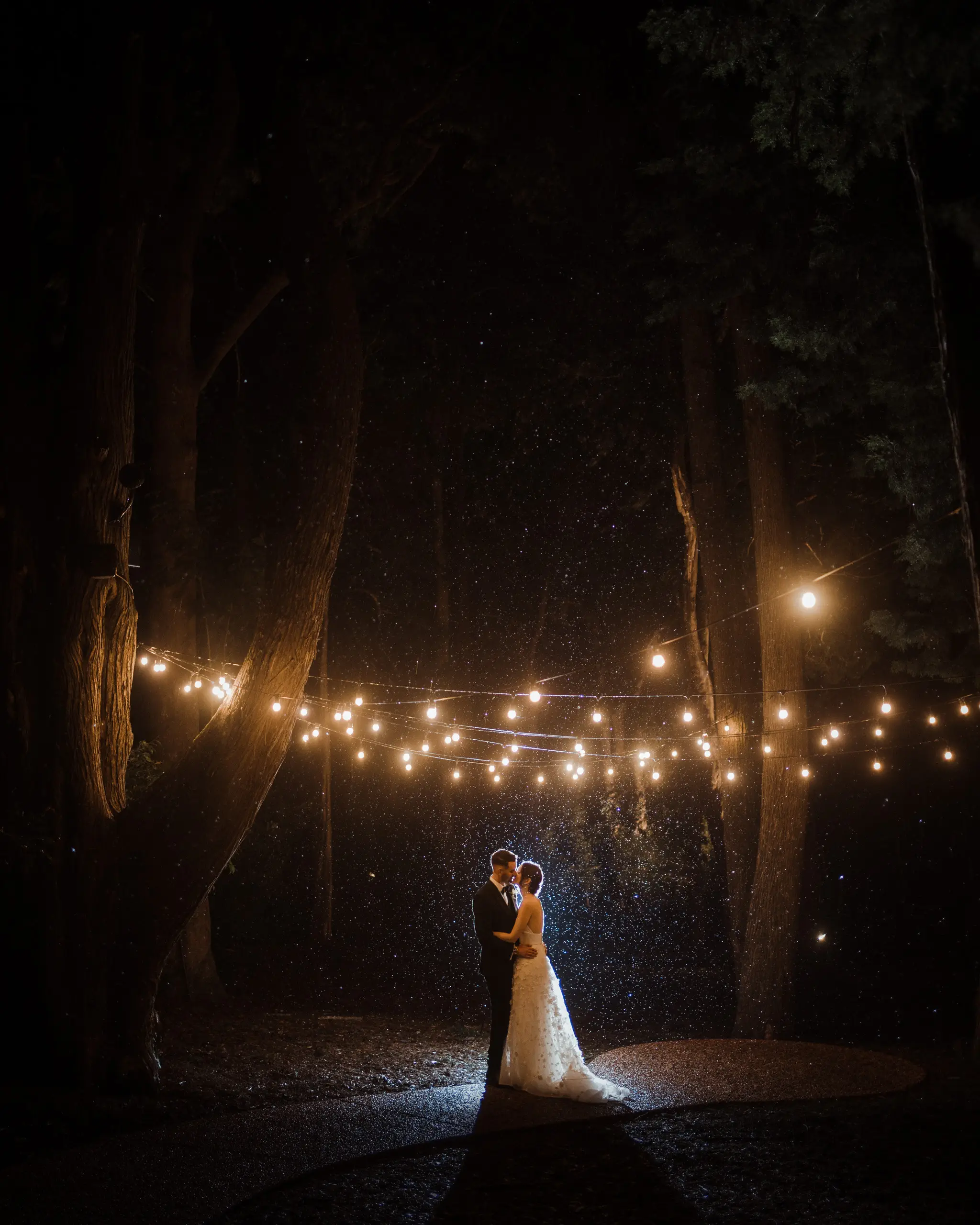 Couple beneath string lights with rain sparking in the flash