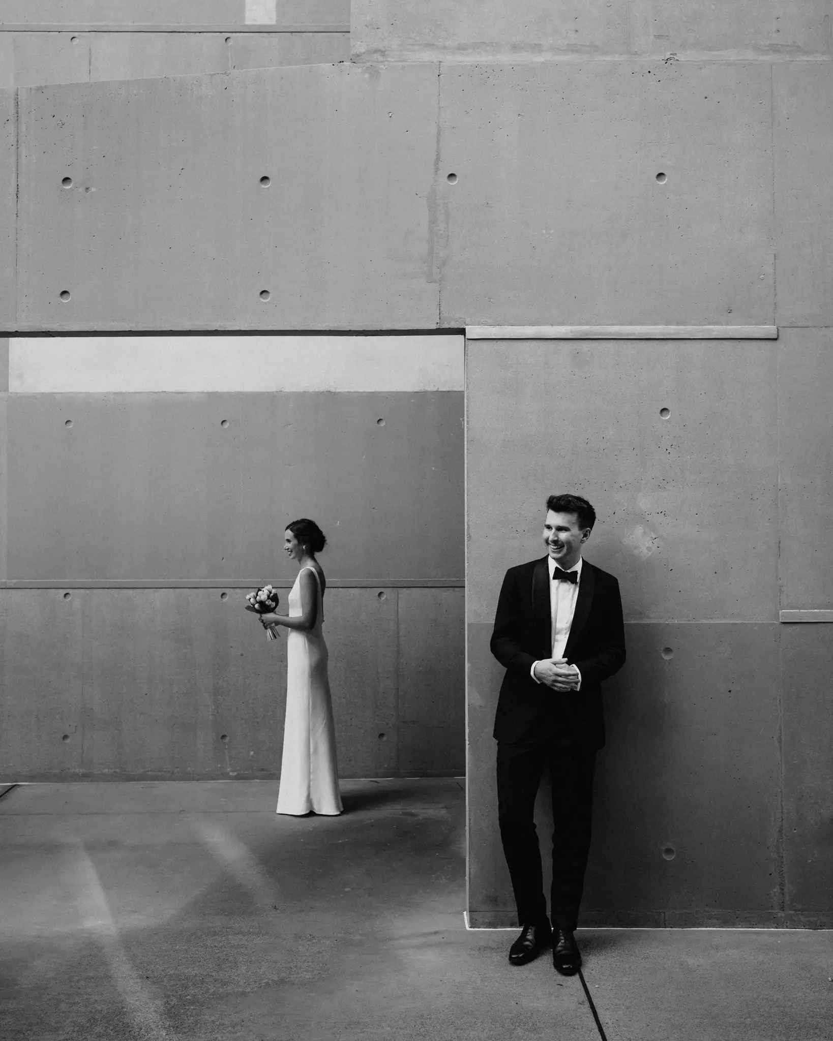 Bride and groom against bare concrete walls, in black and white