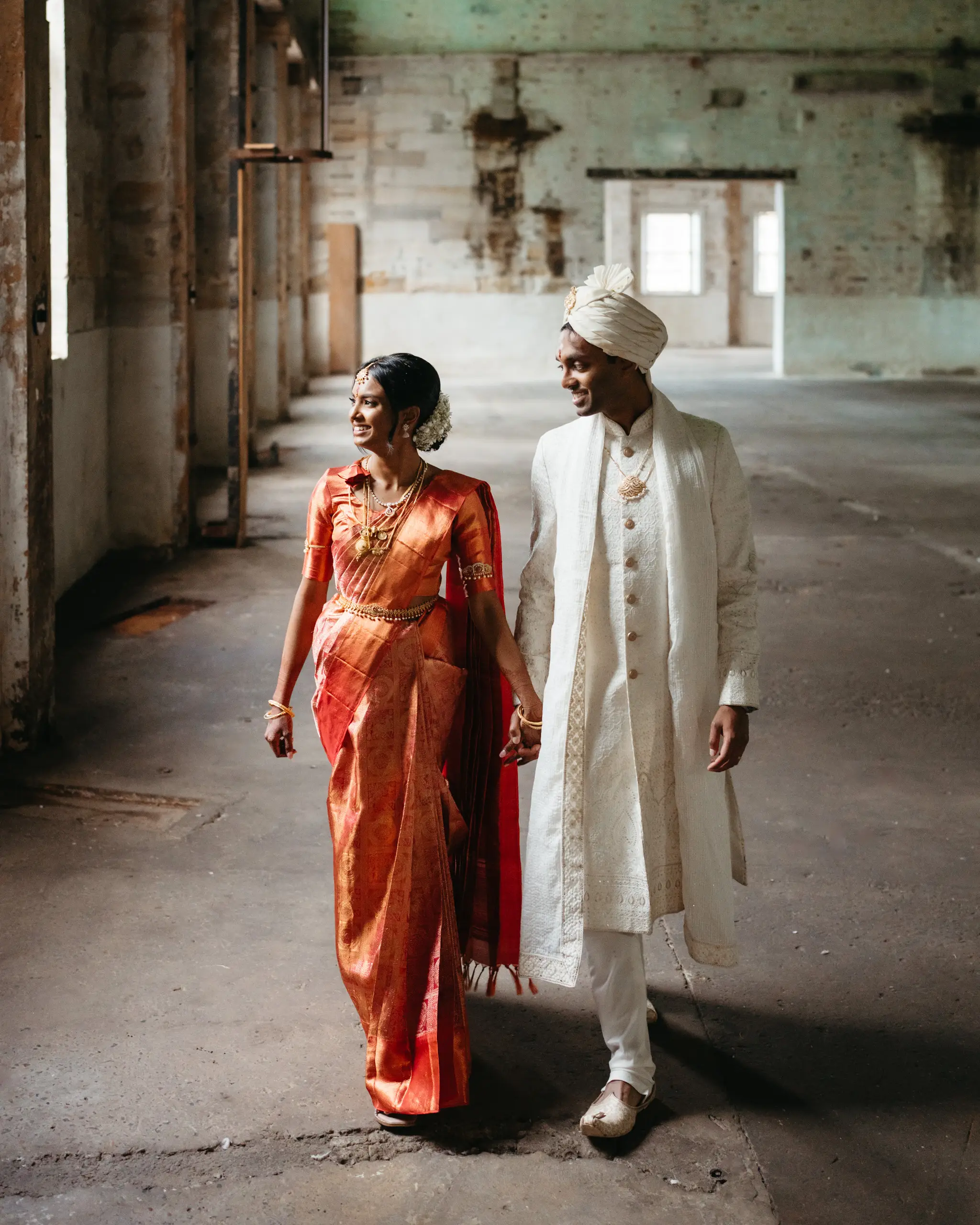 Couple in wedding sherwani and sari walking an old warehouse corridor