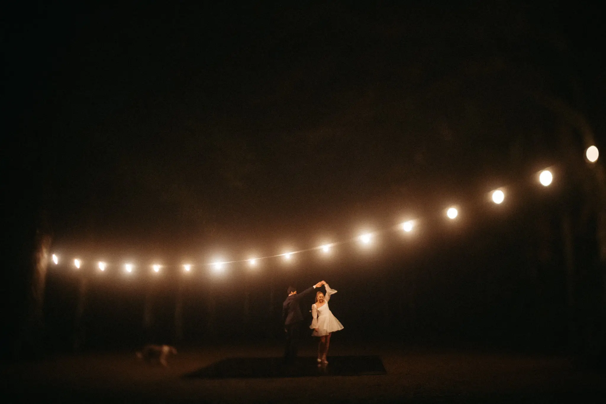 The couple dancing tiny beneath a long string of lights