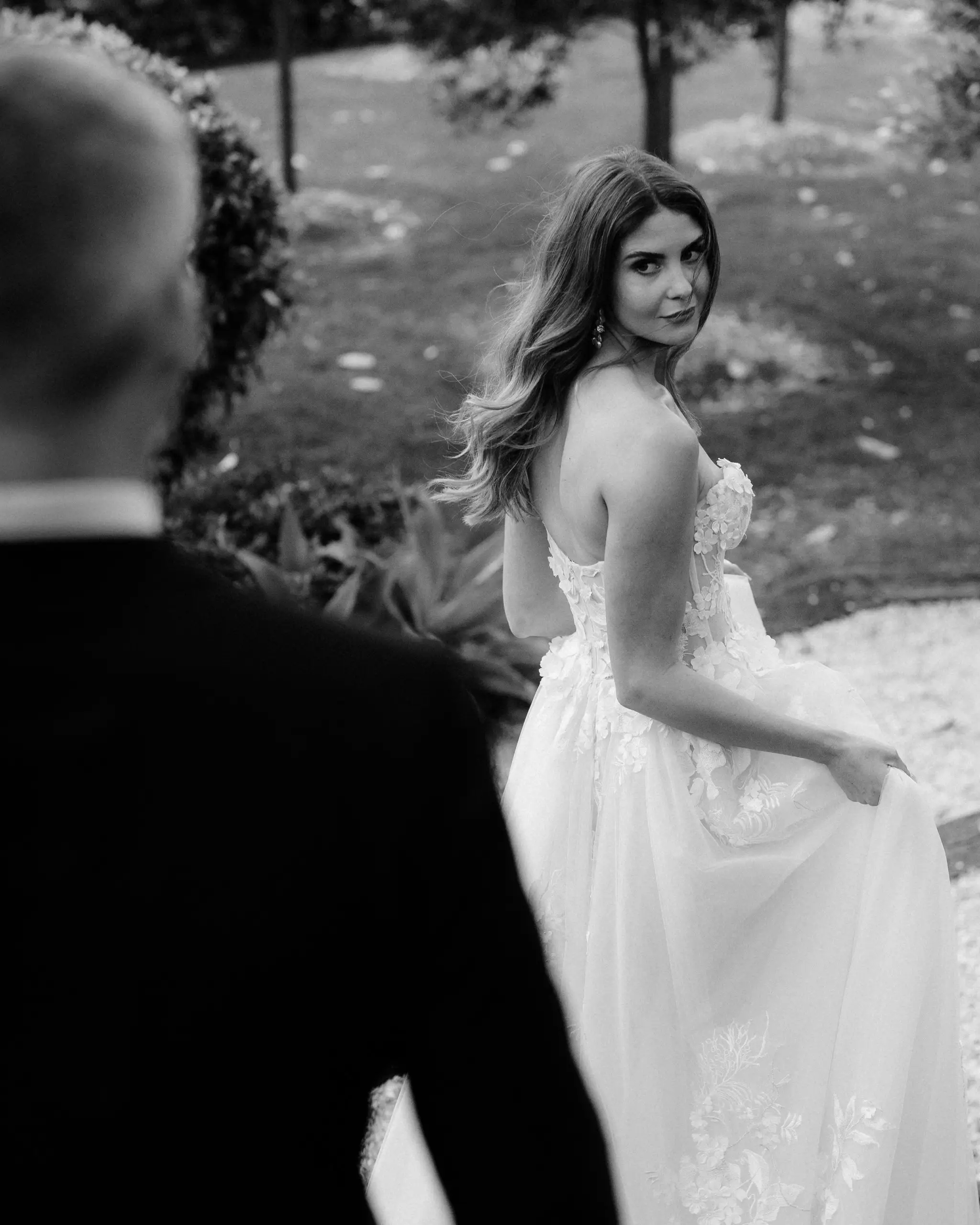 Bride glancing back over her shoulder mid-walk, in black and white