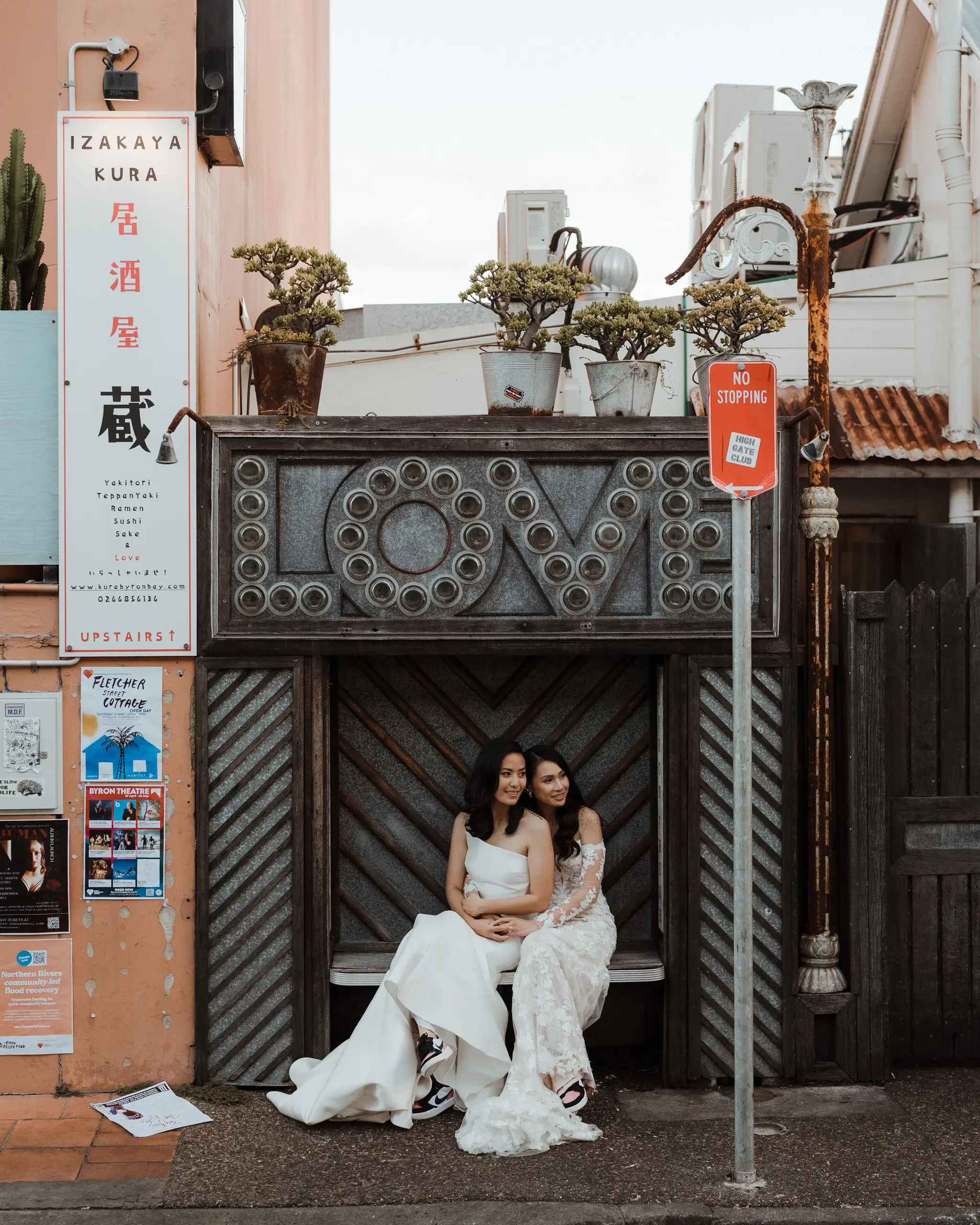 Two brides sharing a bench on a lantern-signed laneway
