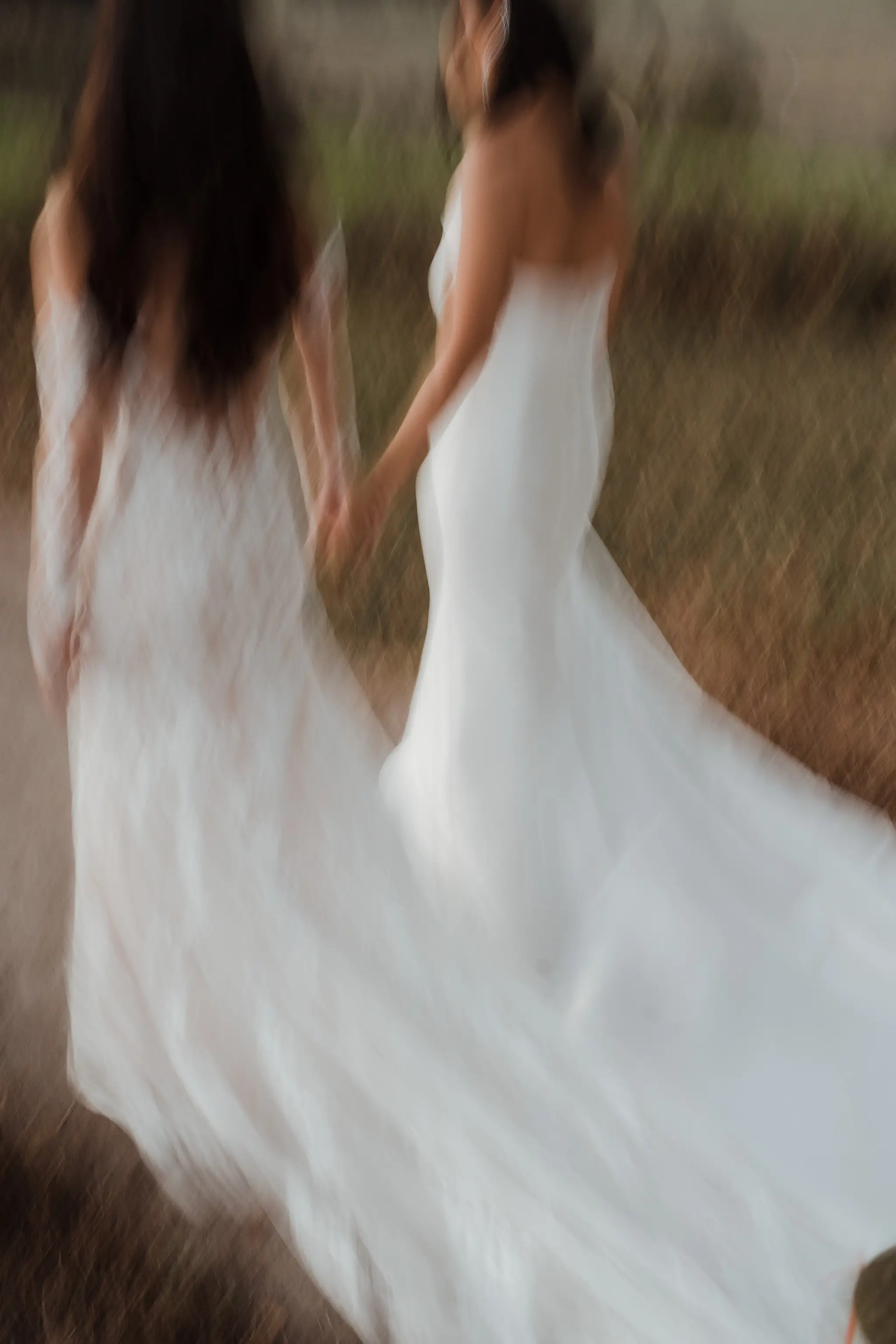 Two brides in motion through the grass, veiled in blur