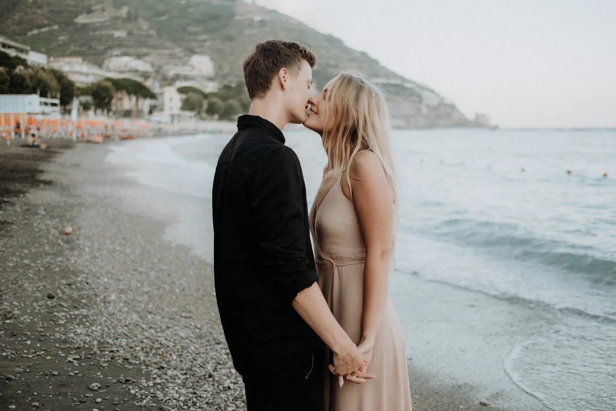 Couple kissing on a pebble beach below a coastal town
