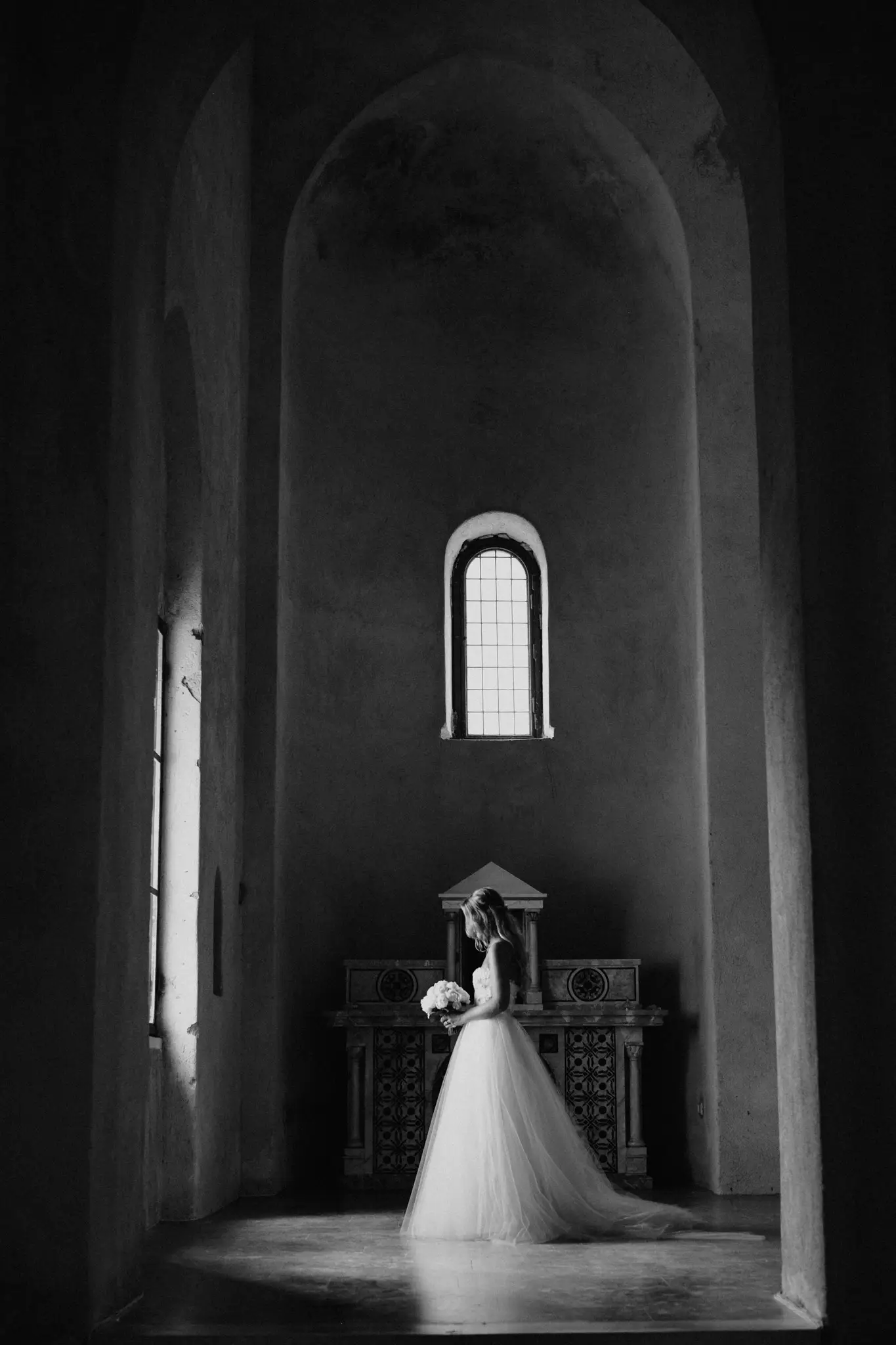 Bride at the altar of a stone chapel, in black and white