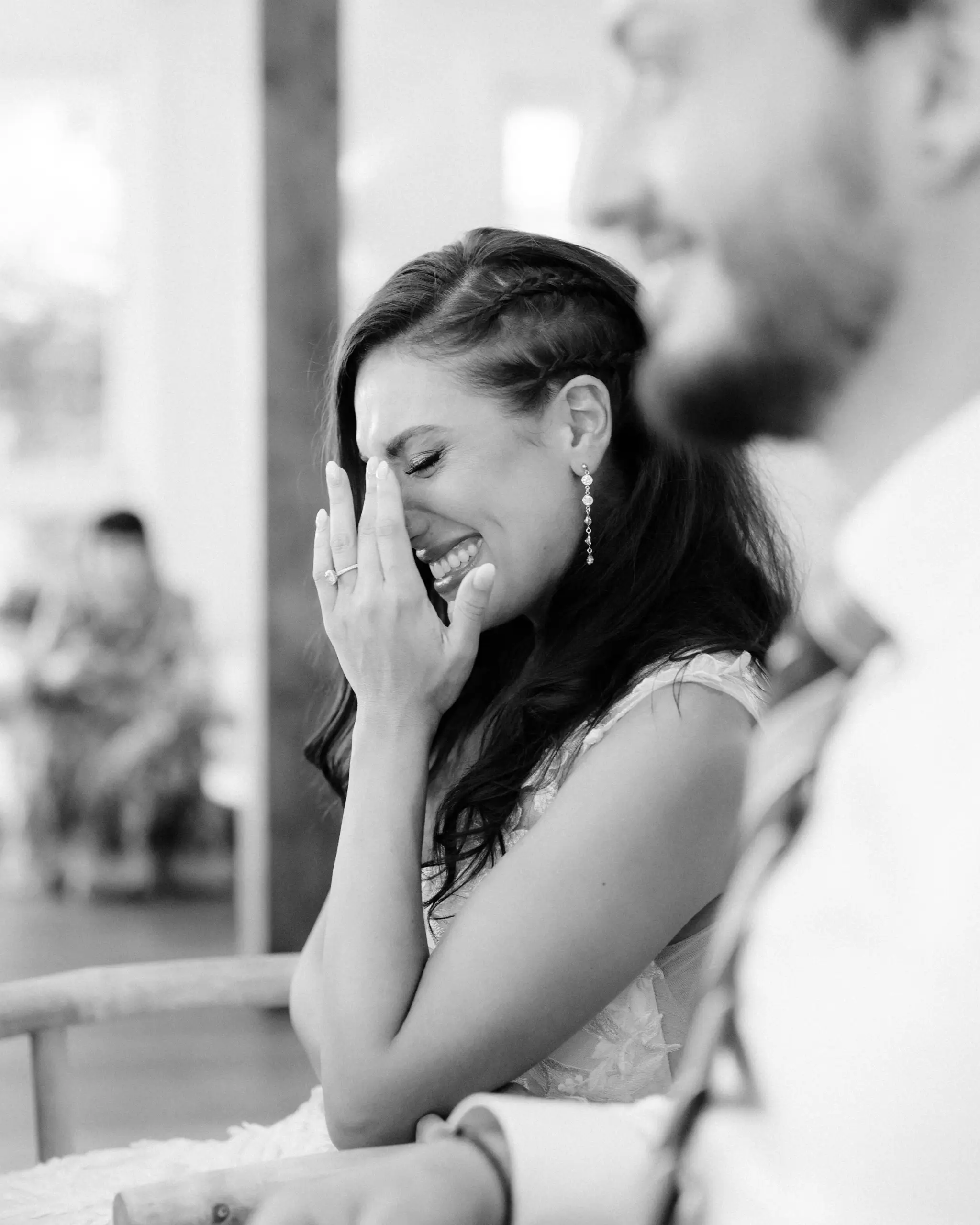 Bride laughing beside the groom during the speeches, in black and white