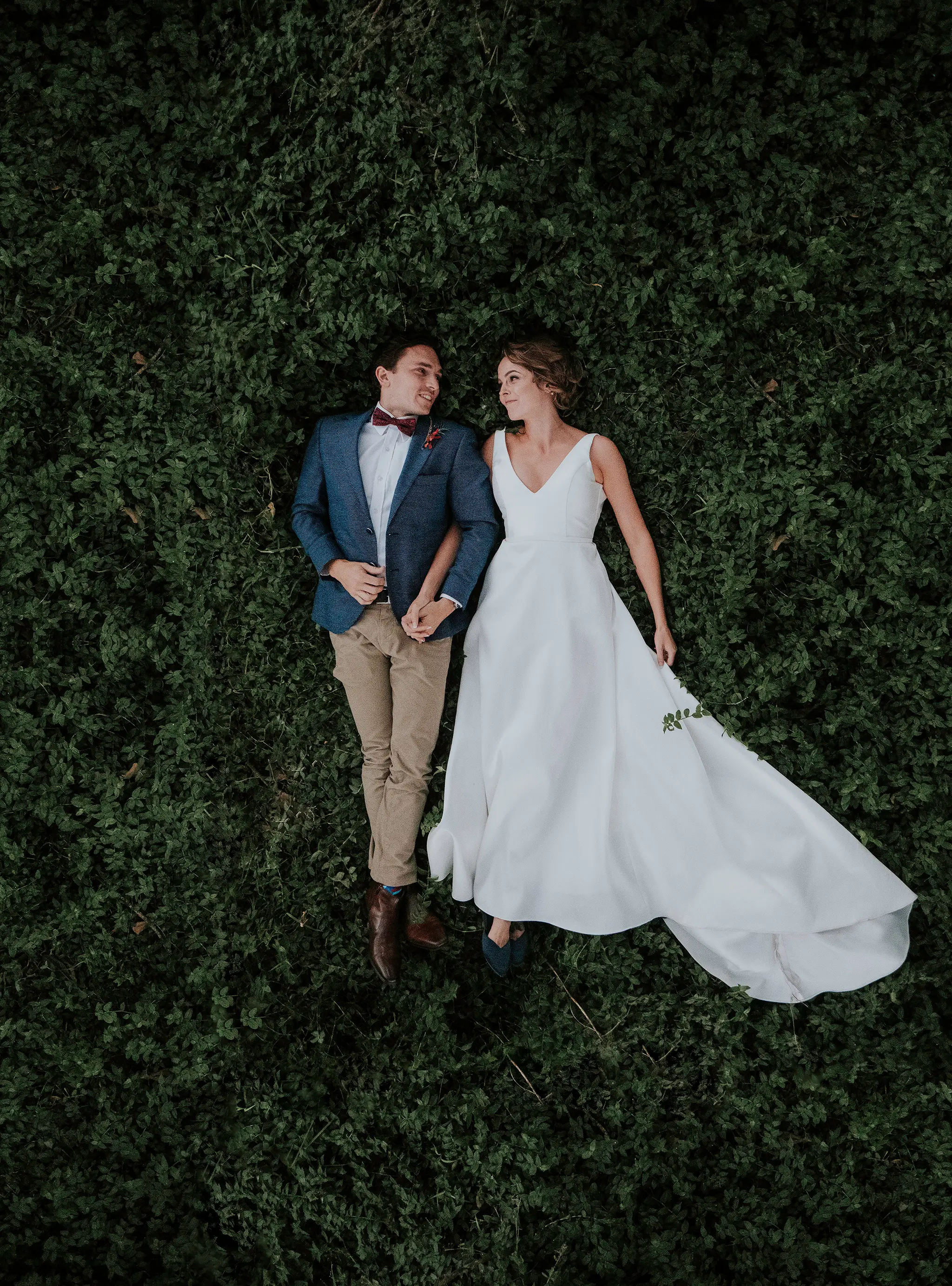 Bride and groom lying hand in hand on the hedge