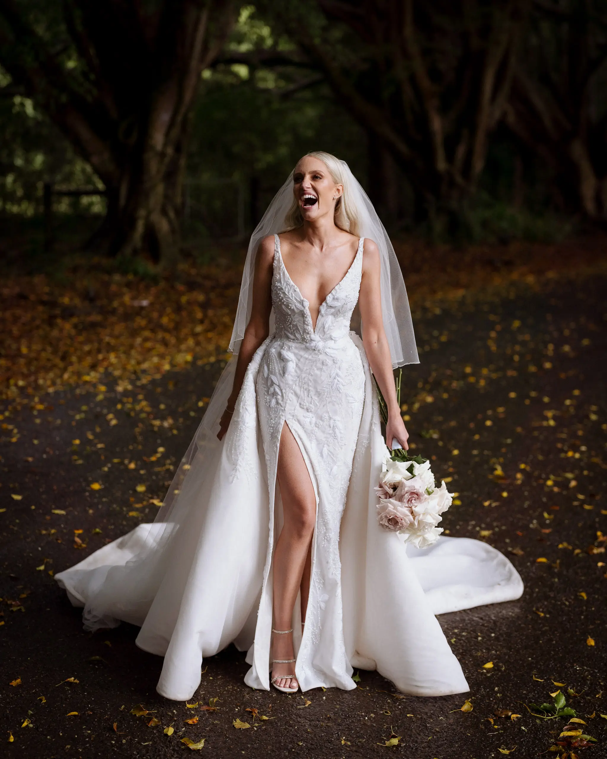 Bride laughing mid-stride on a leaf-littered path