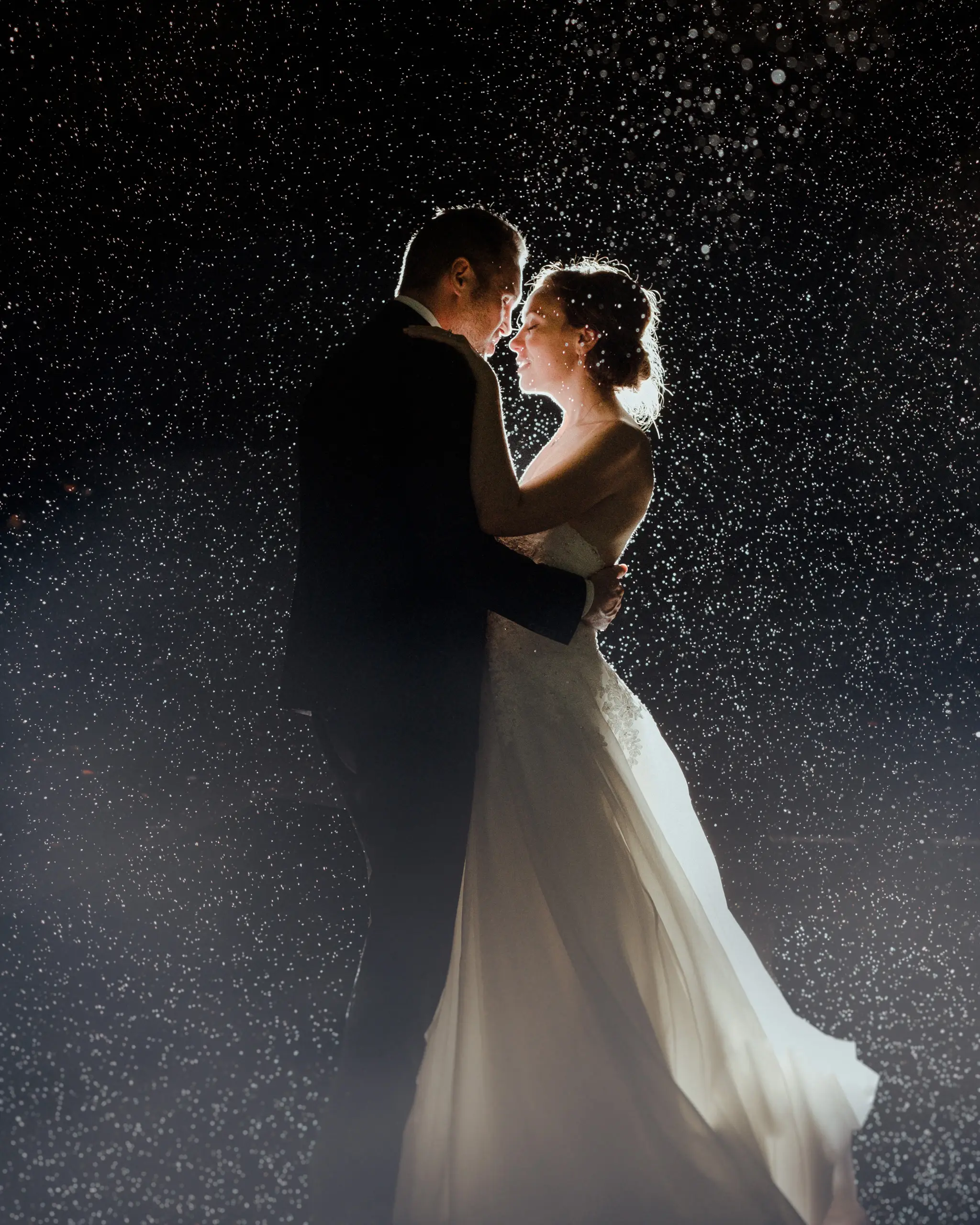 Backlit couple in falling rain at night