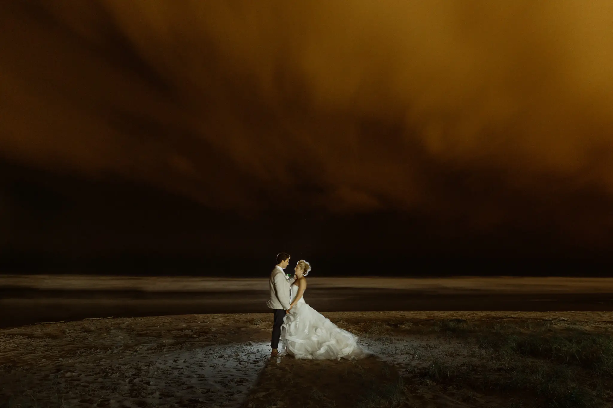 Couple on dark sand under a rust-orange storm sky