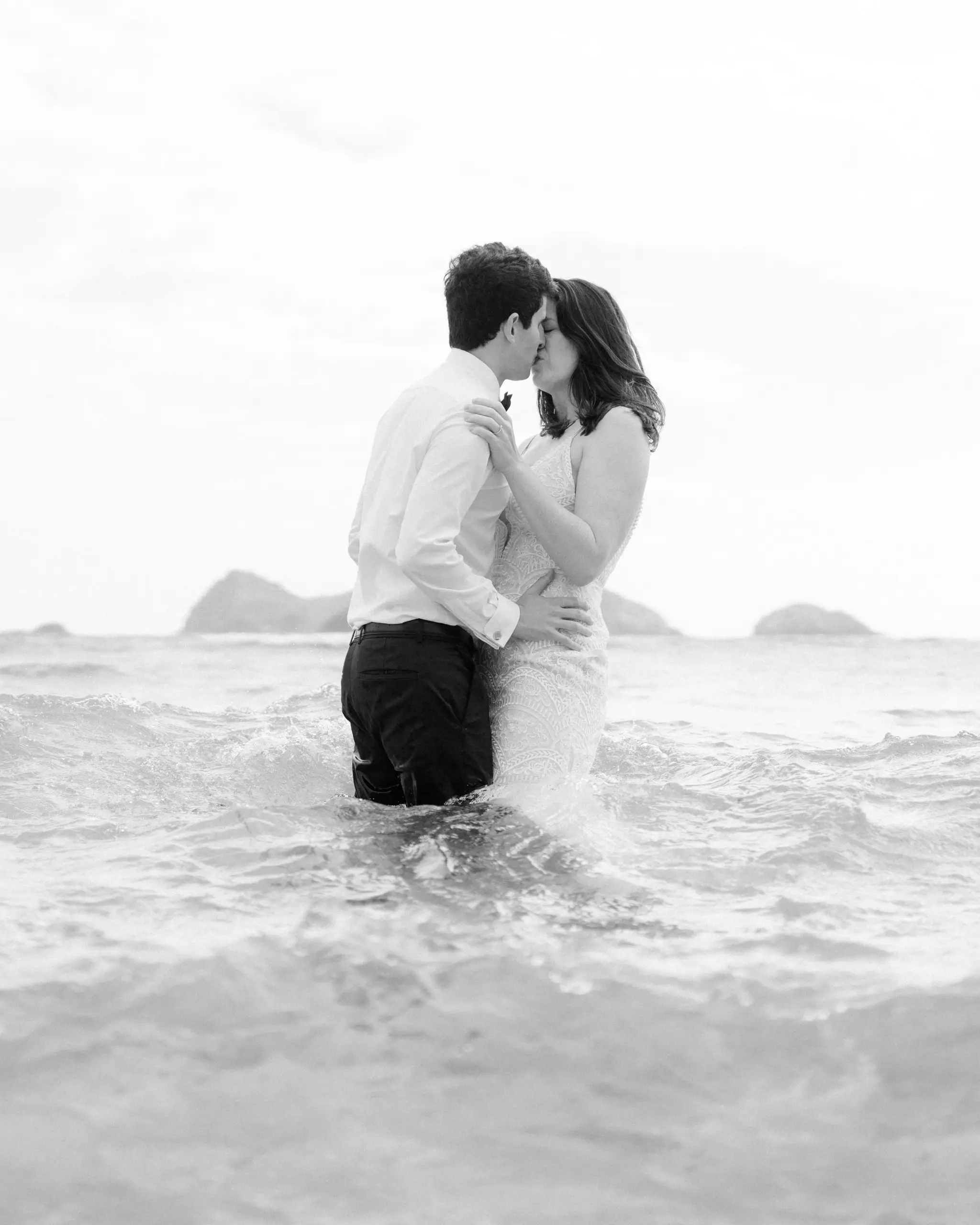 Couple embracing waist-deep in white surf, in black and white