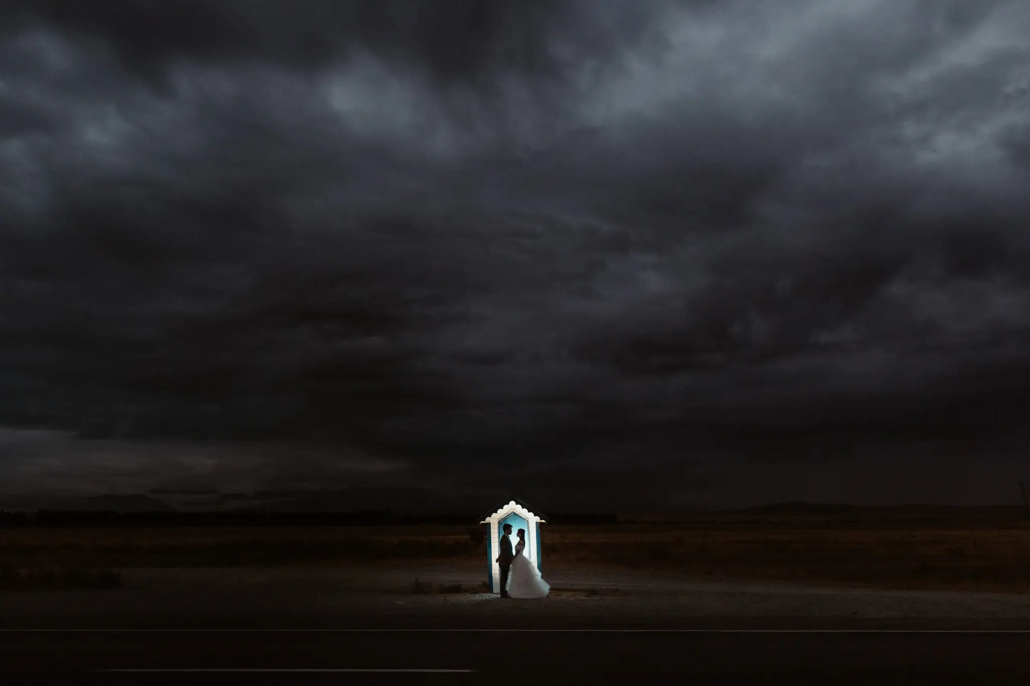 A lone lit beach hut under a black storm sky