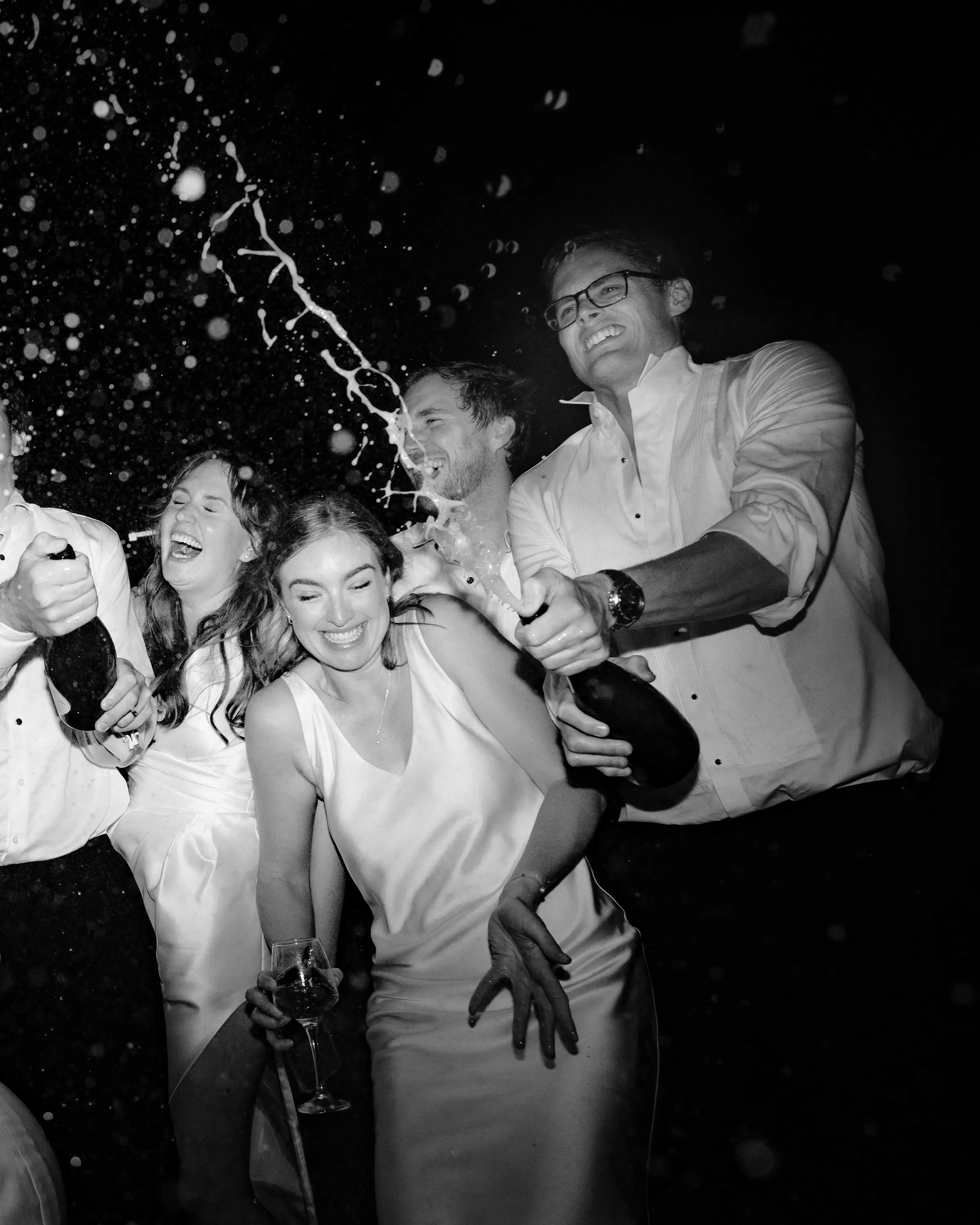 Champagne shaken over the bride on the dance floor, in black and white