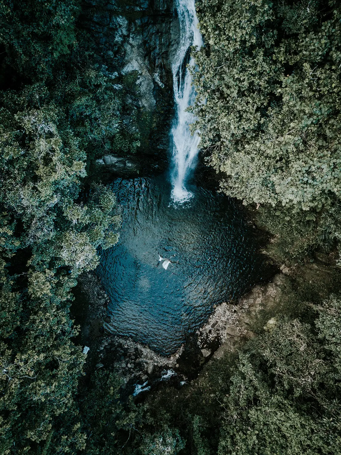Aerial frame of the couple swimming in a waterfall pool