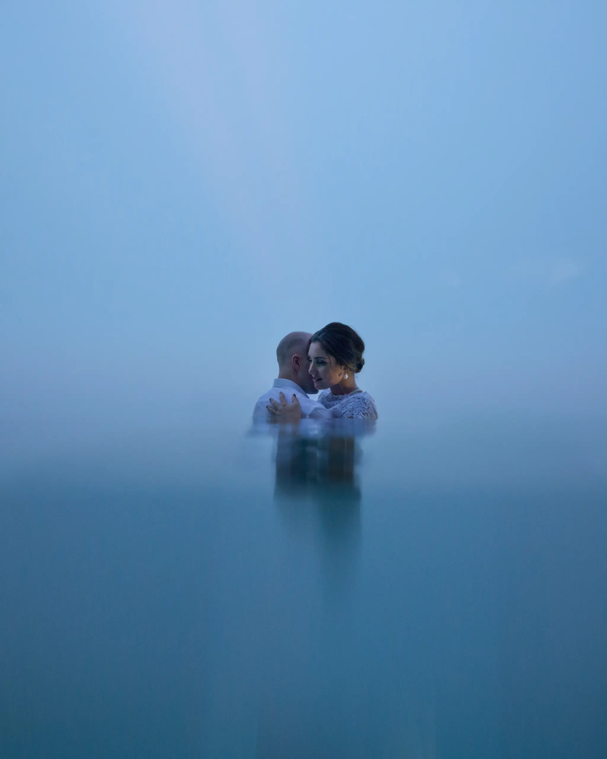 Couple embracing in still blue water, mist behind