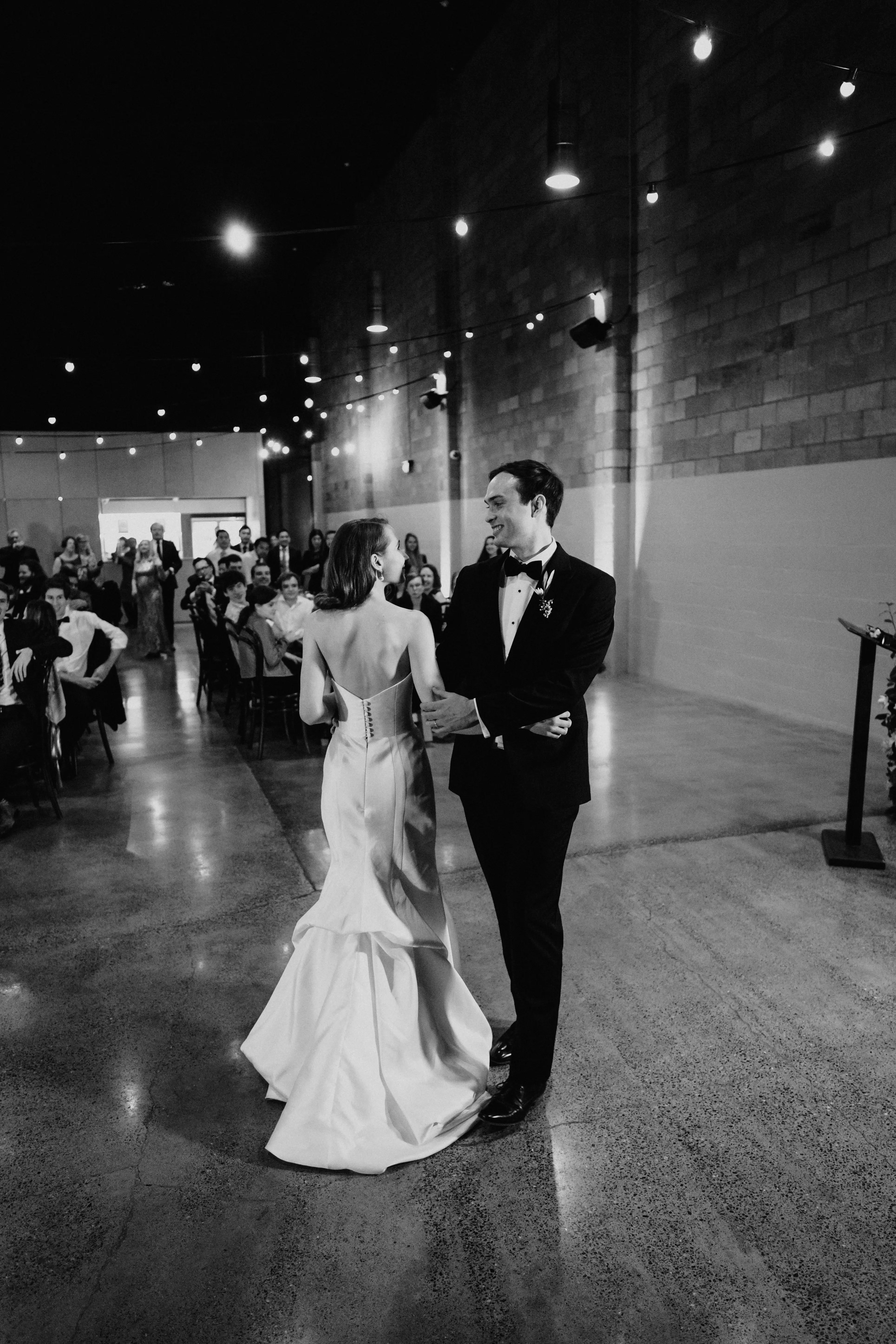 The first dance beneath festoon lights in the brick hall, the guests looking on, Brisbane