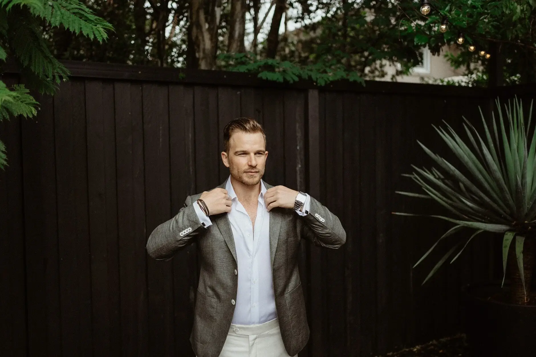 Matt pulling his jacket straight against a dark timber wall, Byron Bay
