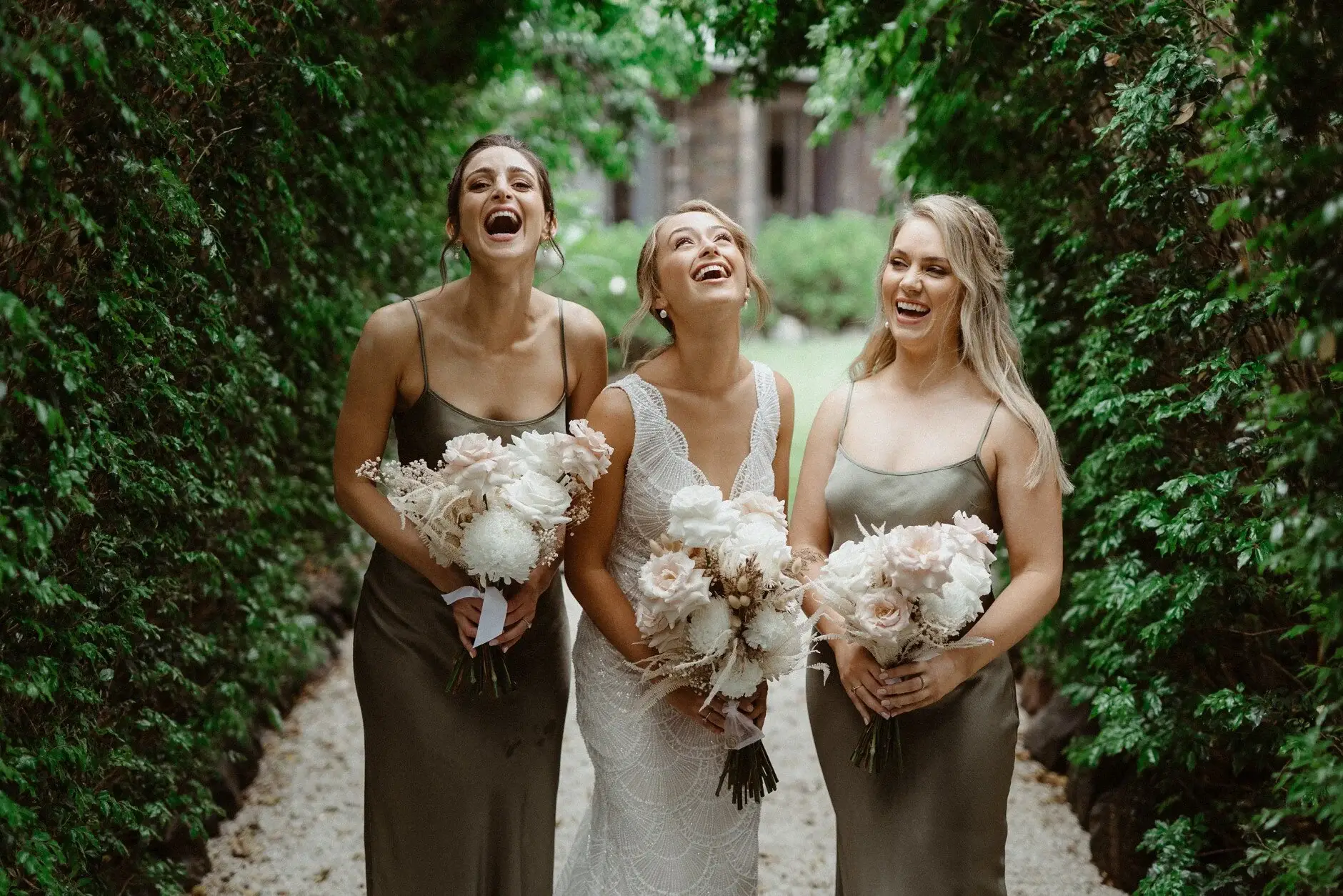 The bridesmaids in olive dresses holding their bouquets in front of a hedge, Byron Bay