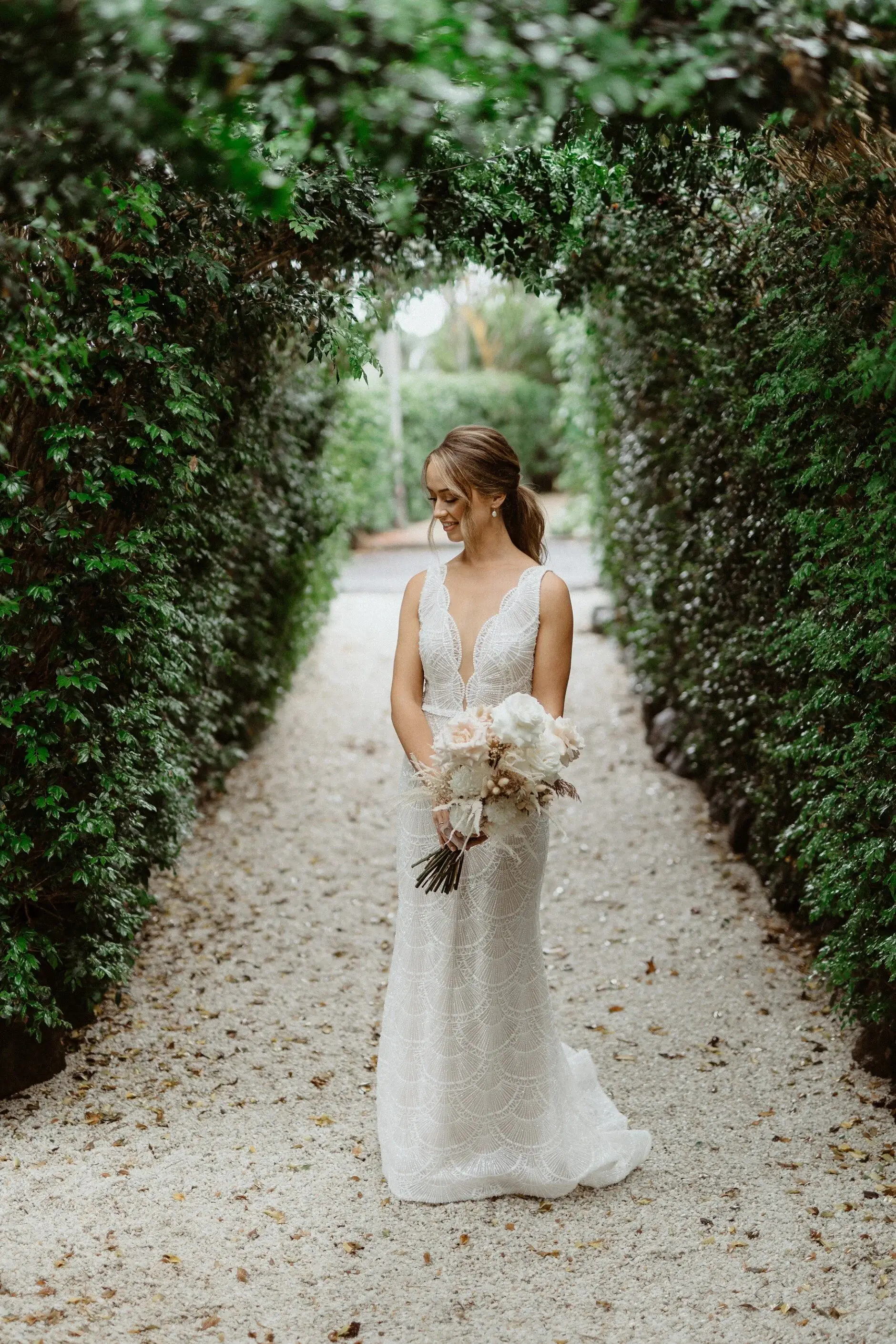 Breanna standing alone at the end of a hedged path with her bouquet, Byron Bay