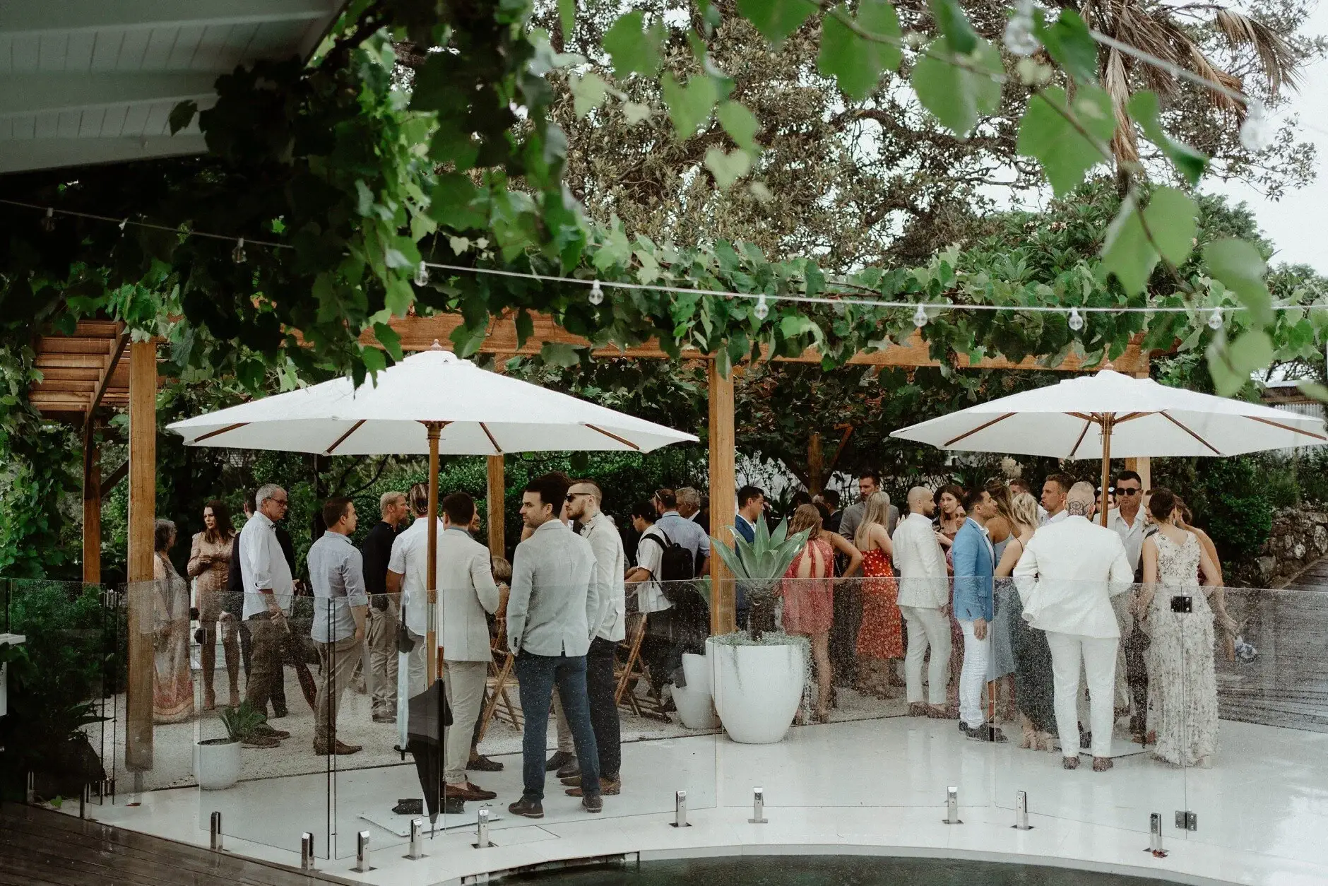 Guests gathering under white umbrellas in the rain before the ceremony, The Fig Tree Byron Bay