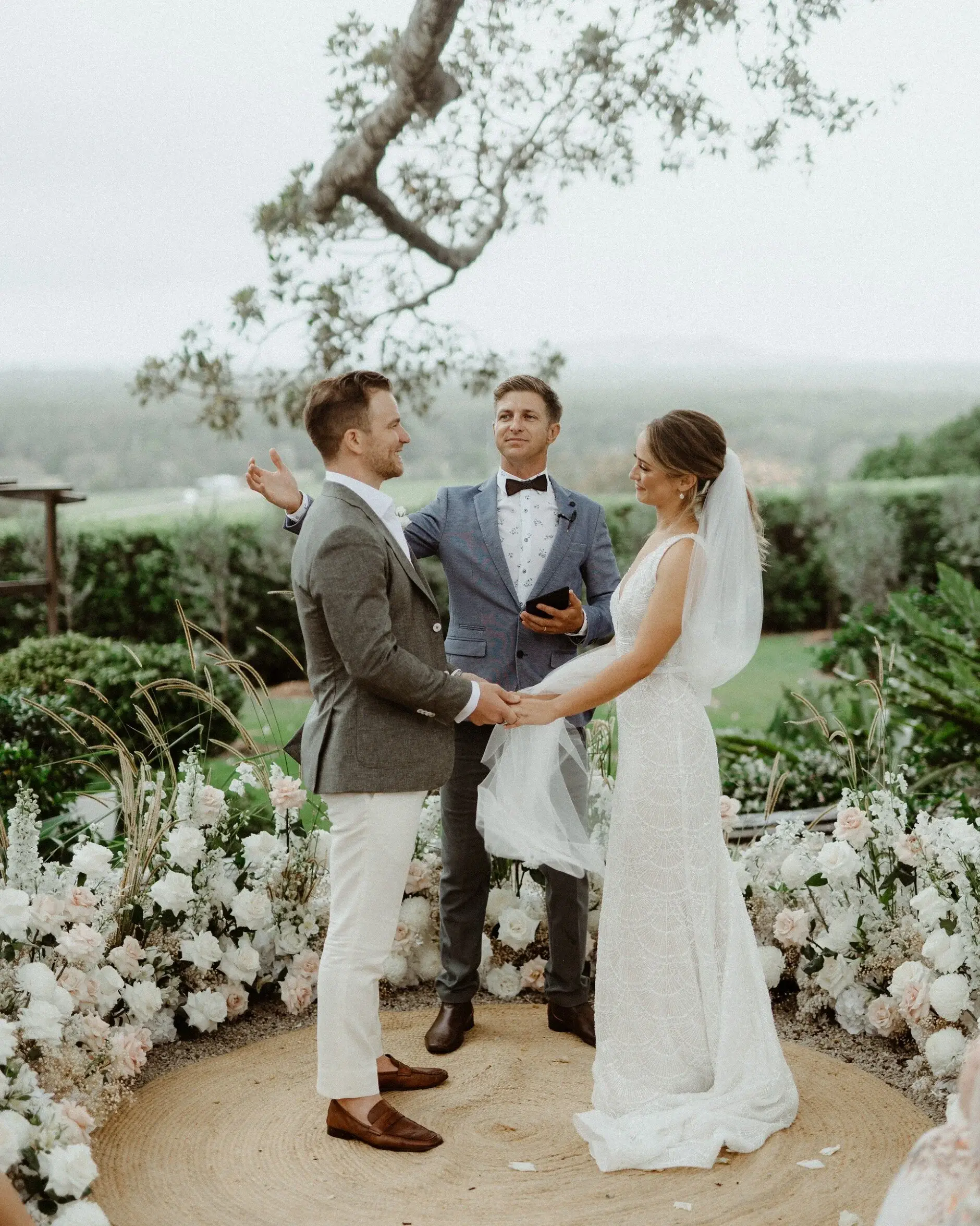Breanna and Matt holding hands during their vows beneath the fig tree, The Fig Tree Byron Bay