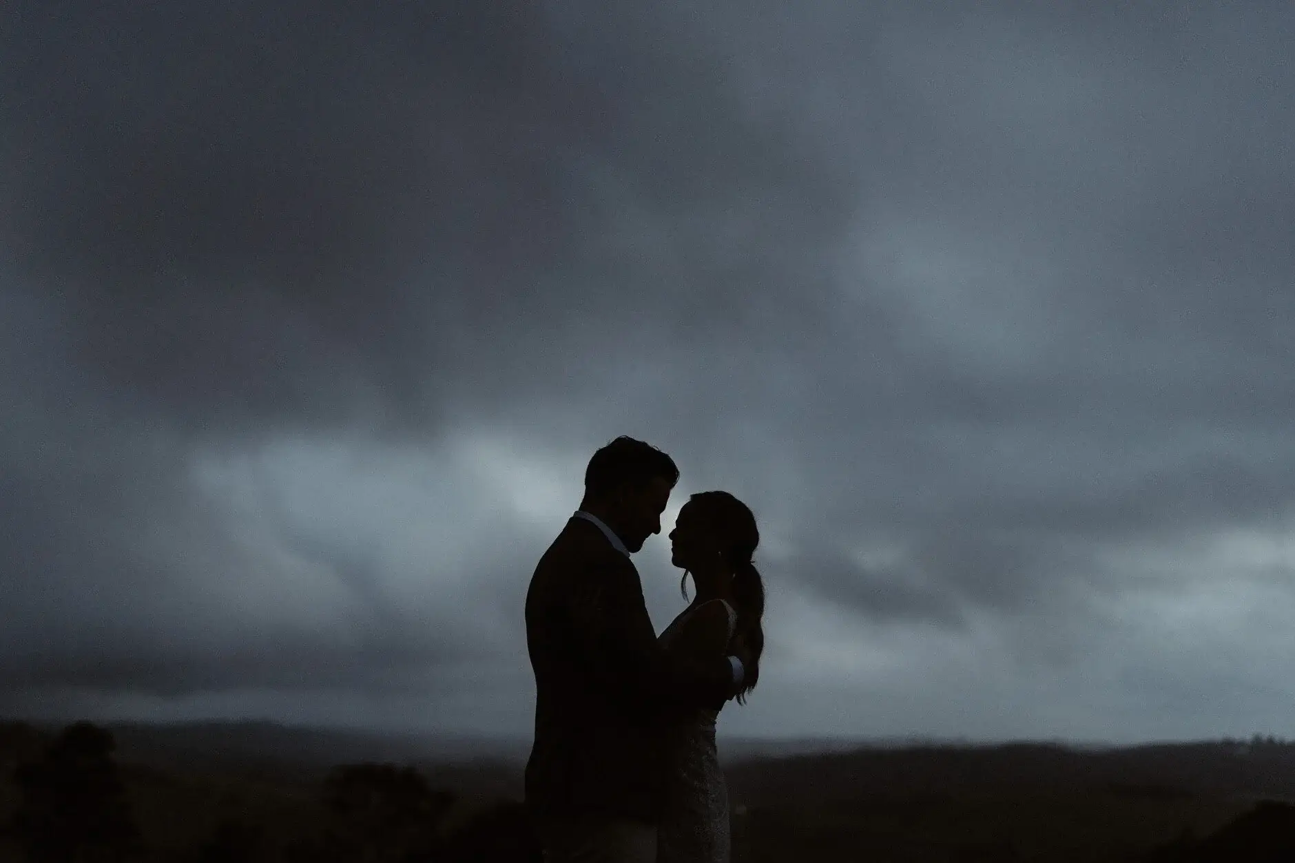 The couple silhouetted against a dark storm sky, Byron View Farm