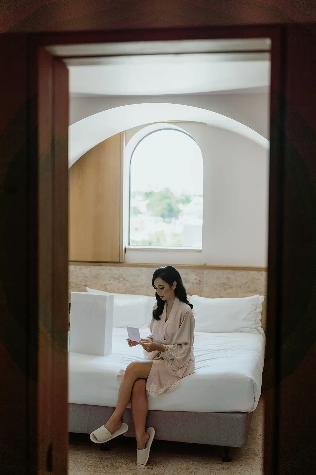 The bride sitting on the bed in her room, framed by the doorway, The Calile Hotel