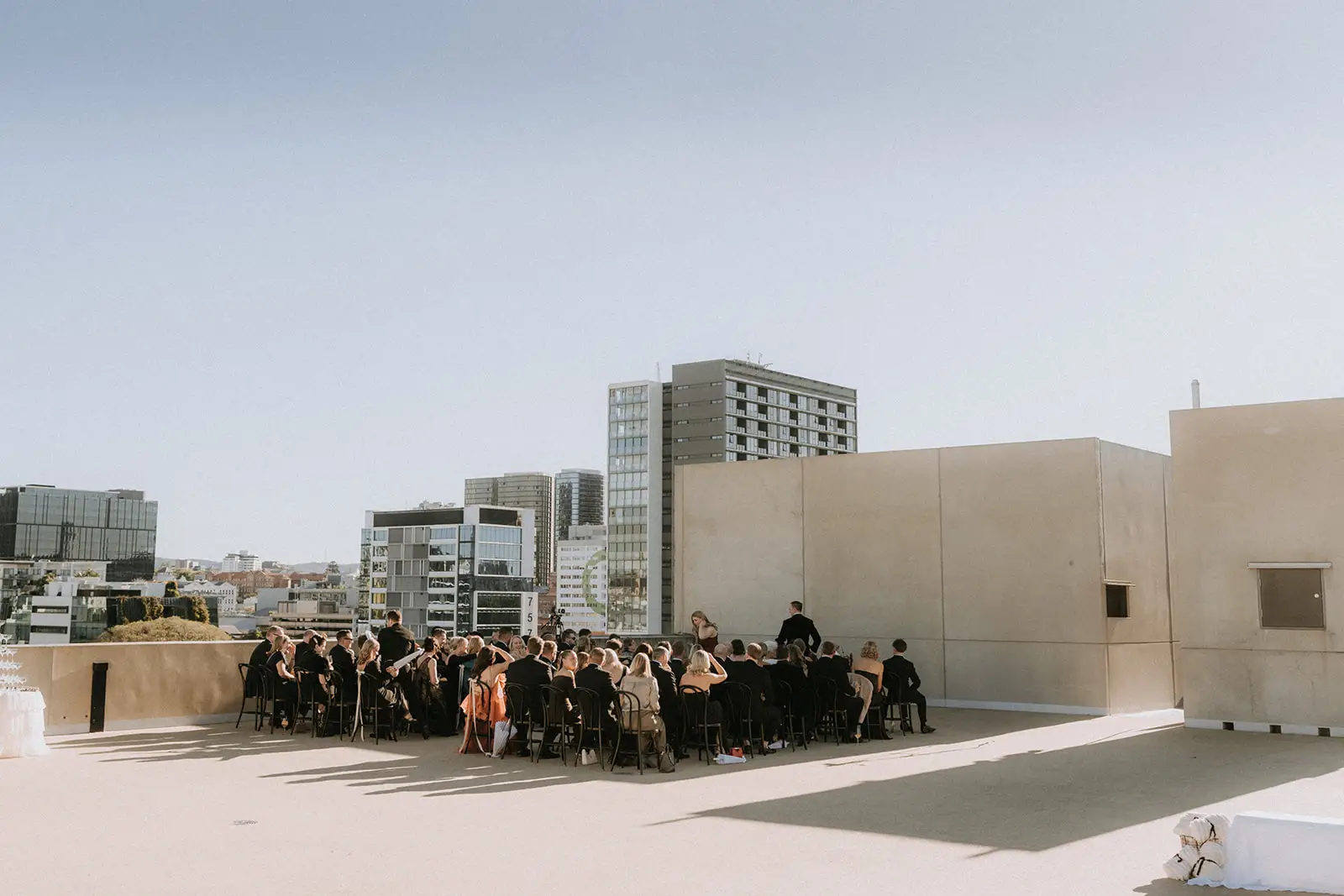 Guests seated for a rooftop ceremony with the city skyline behind, The Calile Hotel