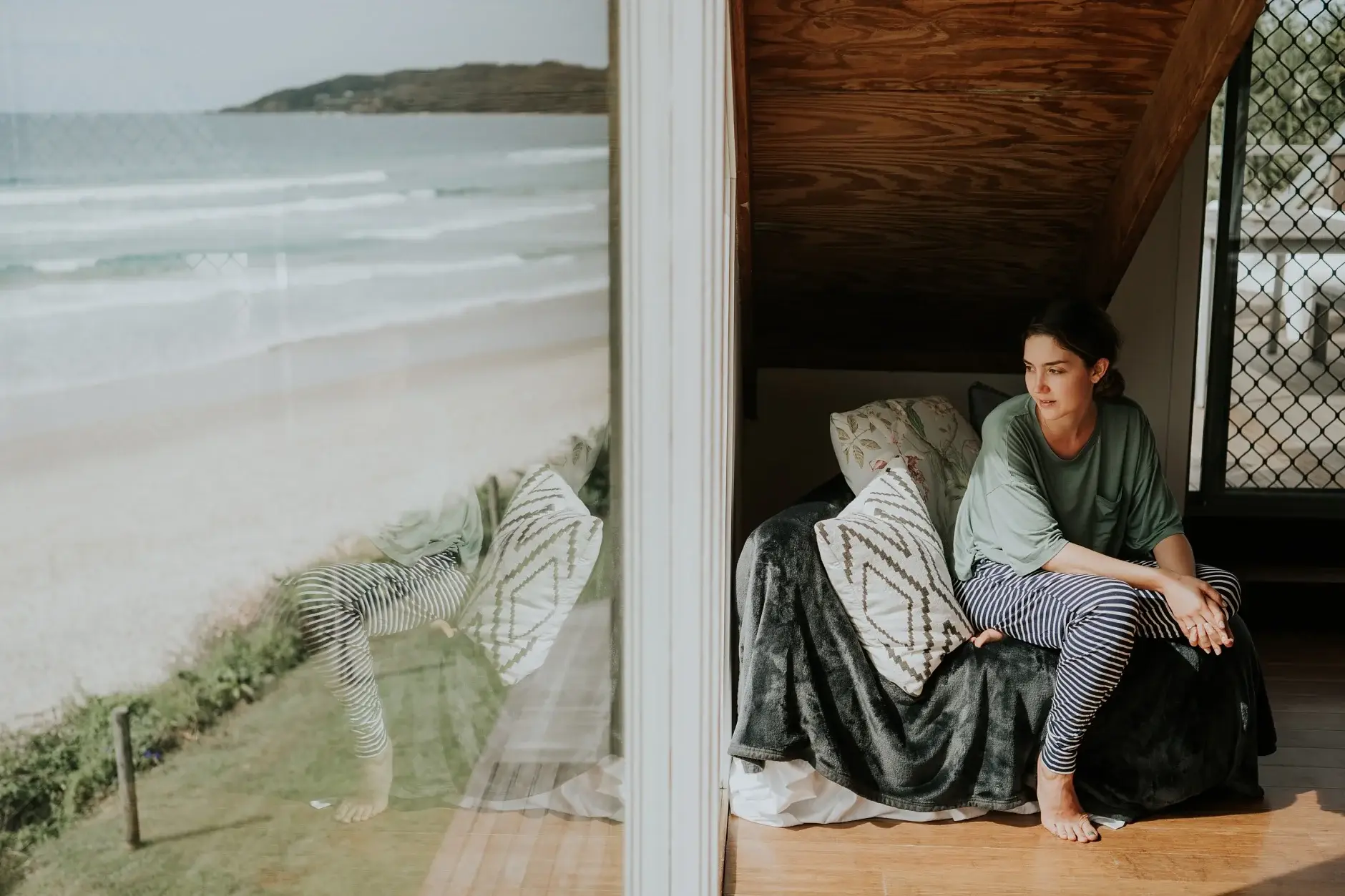 Cassie sitting on the daybed with the beach beyond the open doors, Belongil